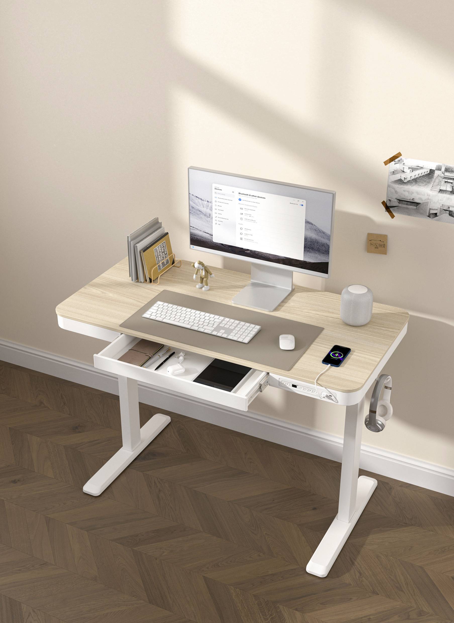 Ein moderner Schreibtisch mit Monitor, Tastatur, Maus und Smartphone. Auf der linken Seite stehen Bücher und rechts hängt ein Bild an der Wand.