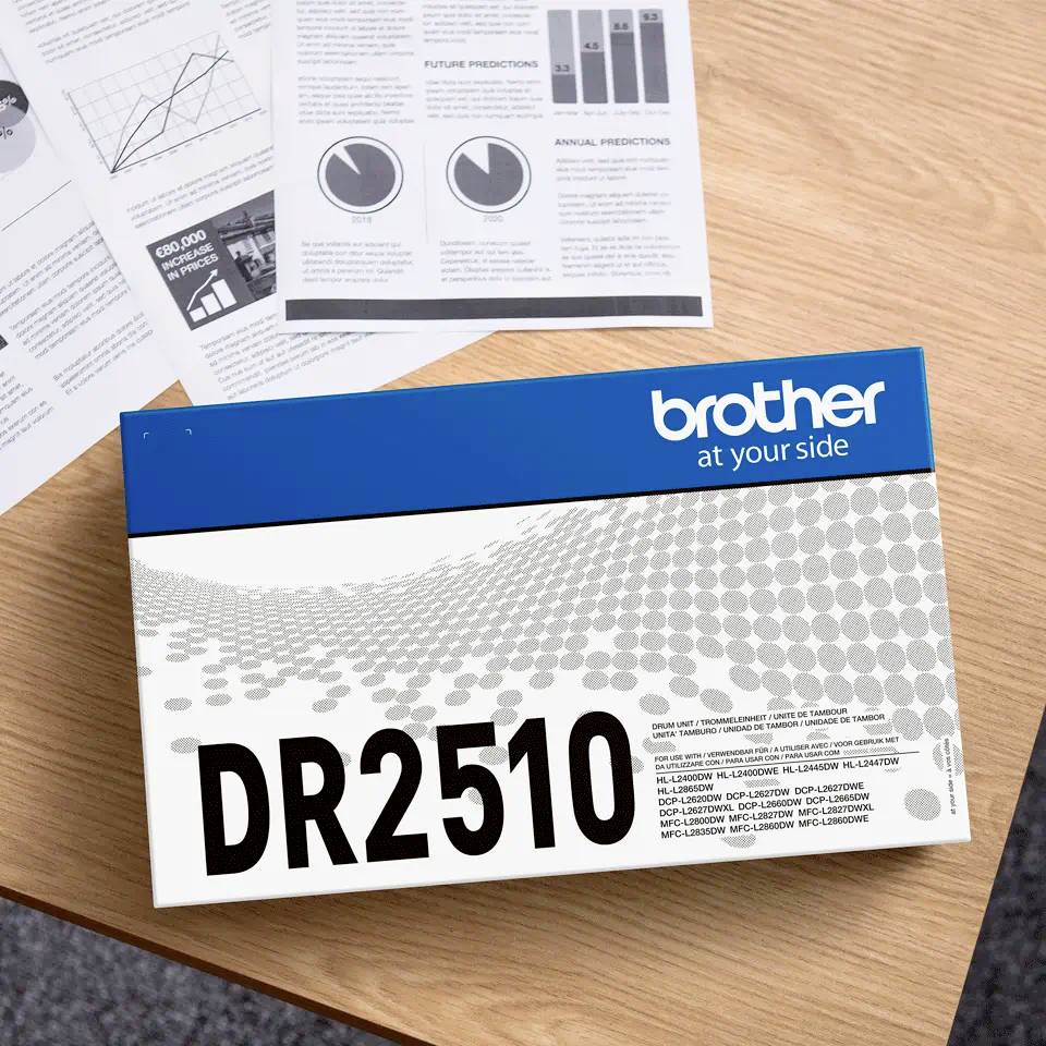 Eine Drucker-Trommeleinheit von Brother, Modell DR2510, liegt auf einem Holztisch. Im Hintergrund liegen mehrere Informationsblätter.