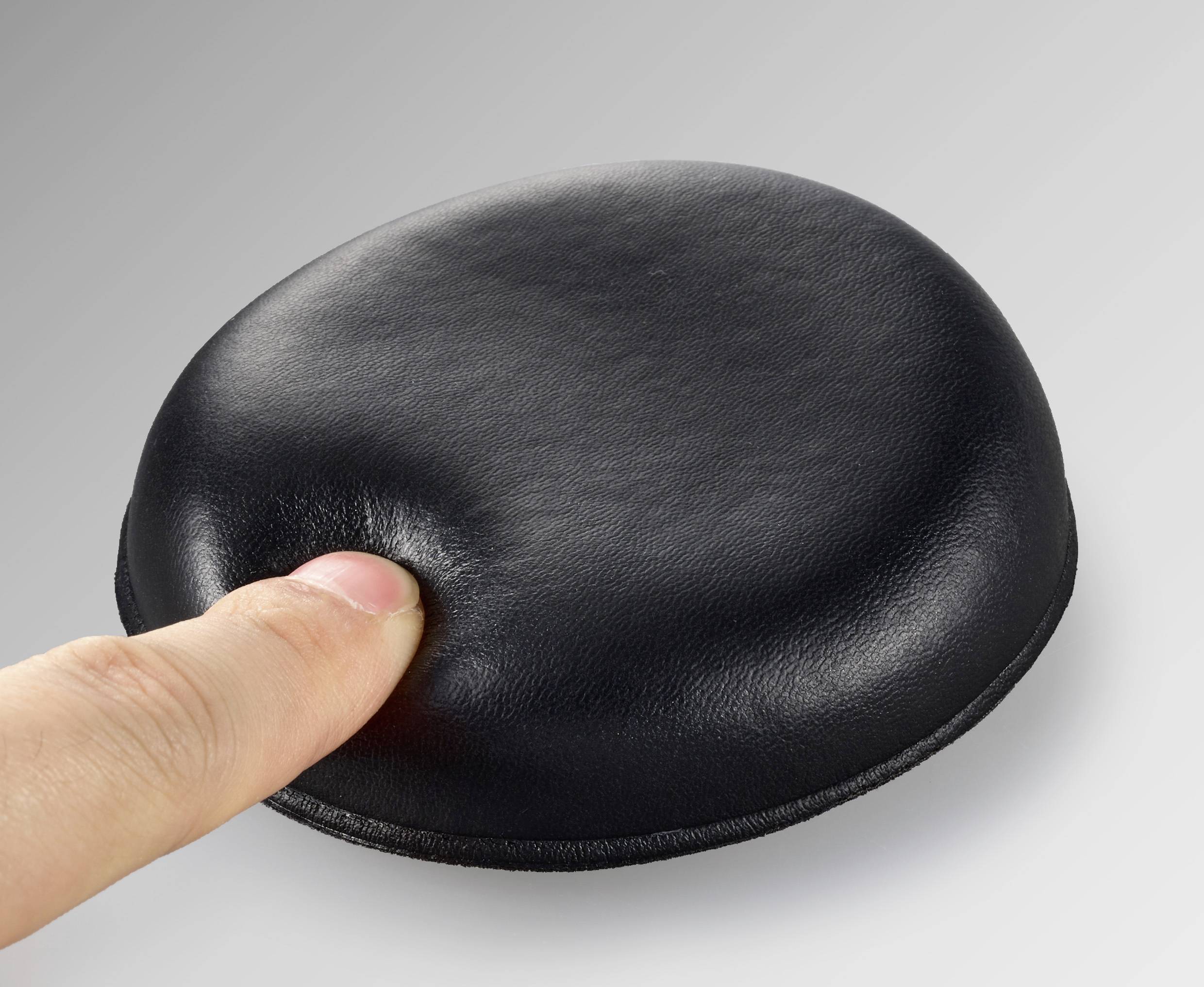 Ein Finger drückt auf ein weiches, schwarzes Polster auf einer grauen Fläche.
