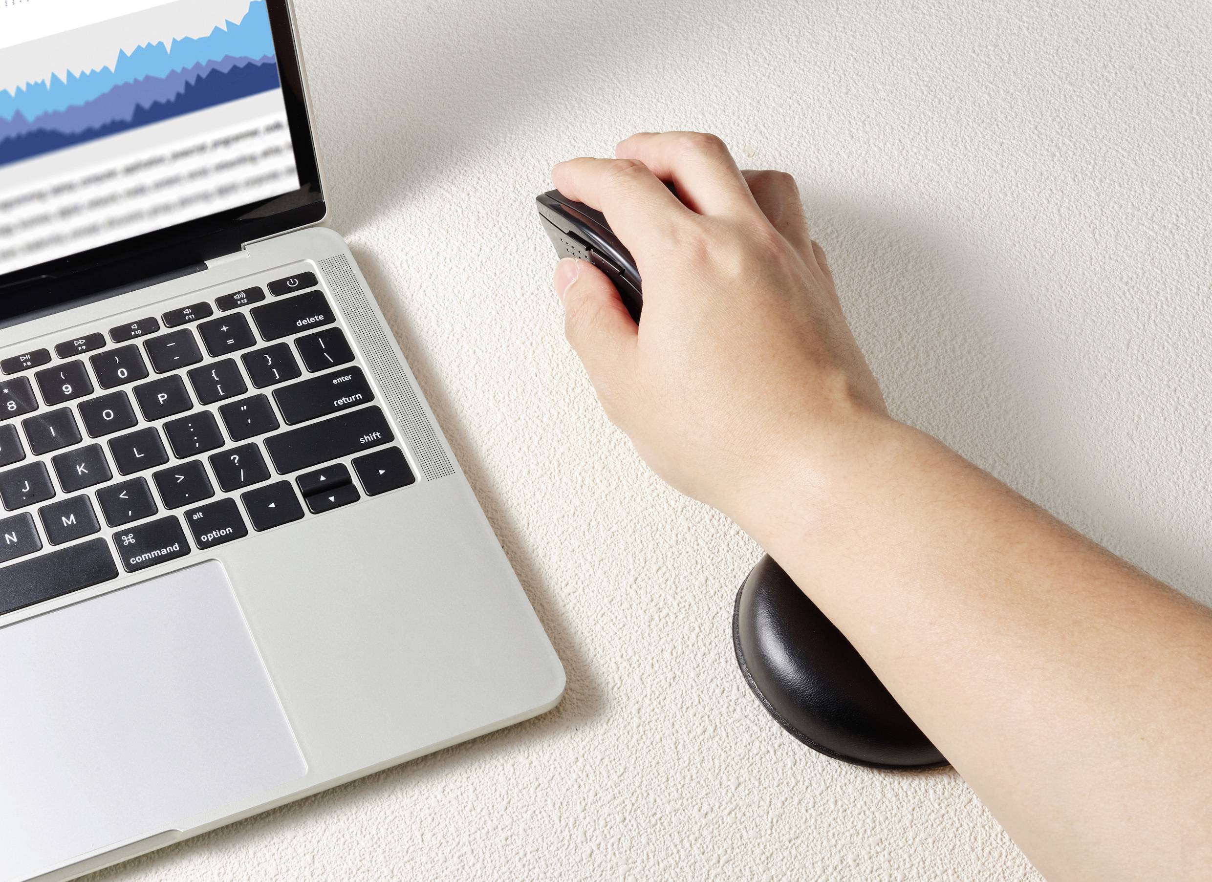 Hand, die eine Computermouse auf einem ergonomischen Mauspad hält; daneben ein Laptop mit einem Diagramm auf dem Bildschirm.