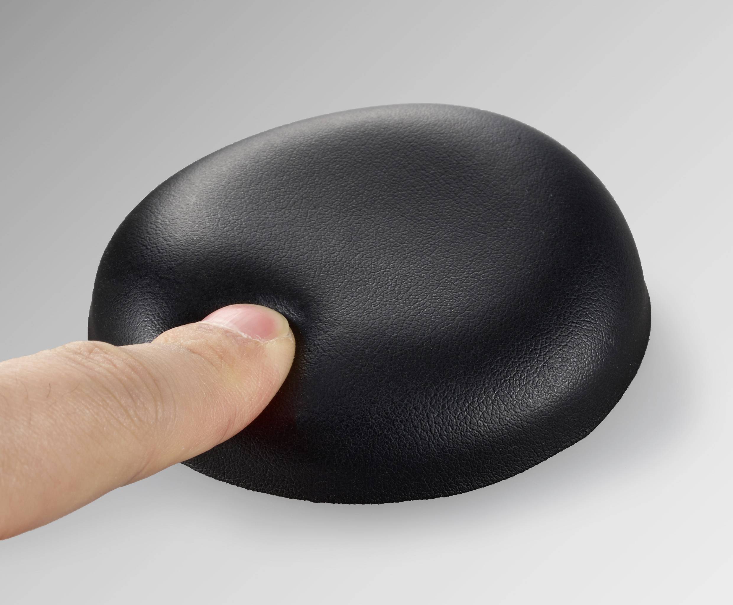 Ein Finger drückt auf ein schwarzes, weiches Kissen, das leicht nachgibt und eine Delle erzeugt.