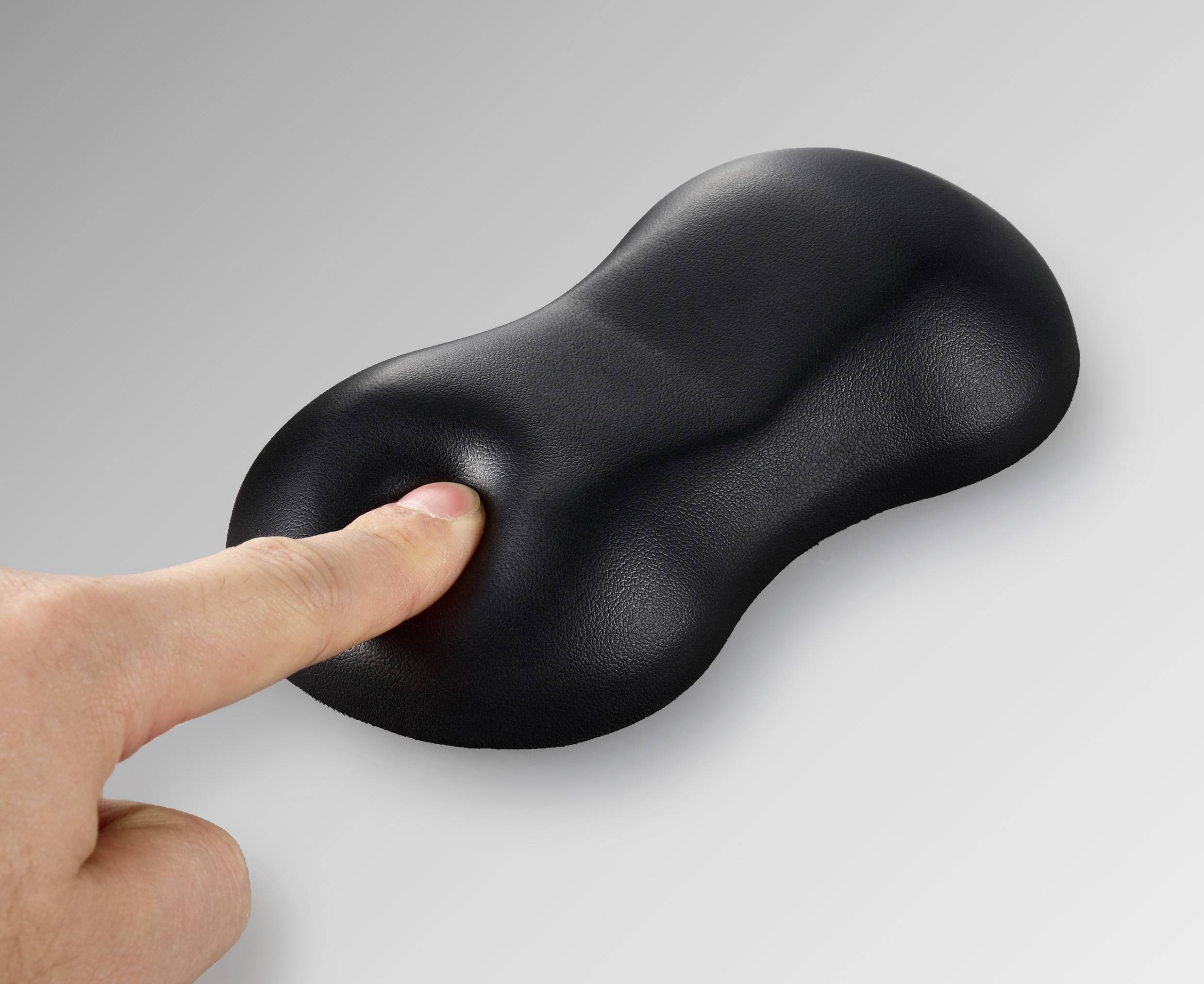 Eine Hand drückt auf ein schwarzes, formbares Kissen, das sich elastisch verformt. Das Kissen hat eine glatte Oberfläche.