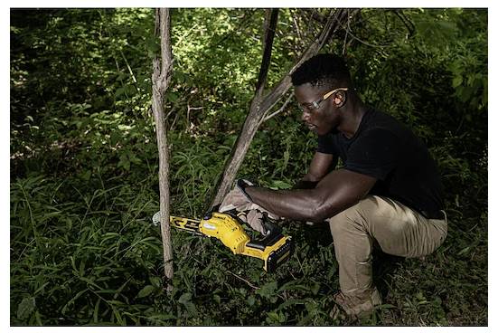 Person, die in einem Wald einen Ast mit einer Säge schneidet und dabei Sicherheitsbrille und Handschuhe trägt, umgeben von grünem Blattwerk.