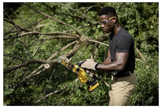 Eine Person mit Sicherheitsbrille und Handschuhen verwendet eine gelbe elektrische Säge, um Äste in einem bewaldeten Gebiet zu schneiden.