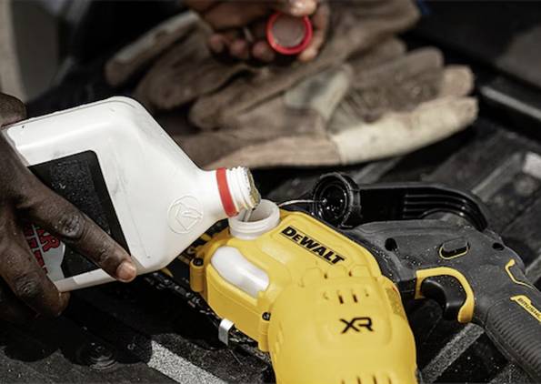 Eine Person gießt Öl in ein gelbes Dewalt-Arbeitsgerät und bereitet es für den Einsatz vor. Arbeitshandschuhe und eine rote Kappe sind im Hintergrund sichtbar.