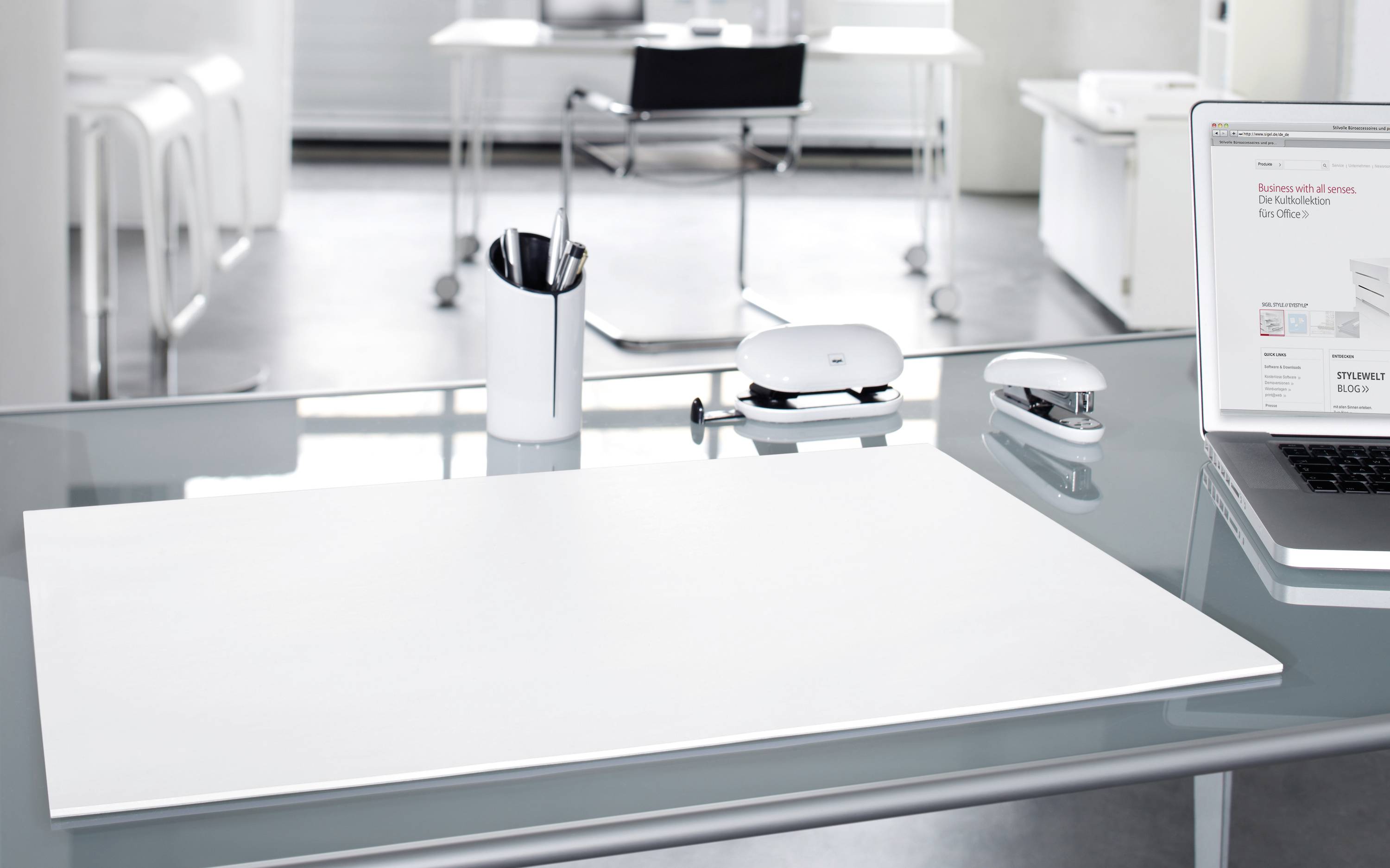 Ein moderner, aufgeräumter Schreibtisch mit Laptop, Schreibutensilien und leerem Notizblock in einem hellen Büro.