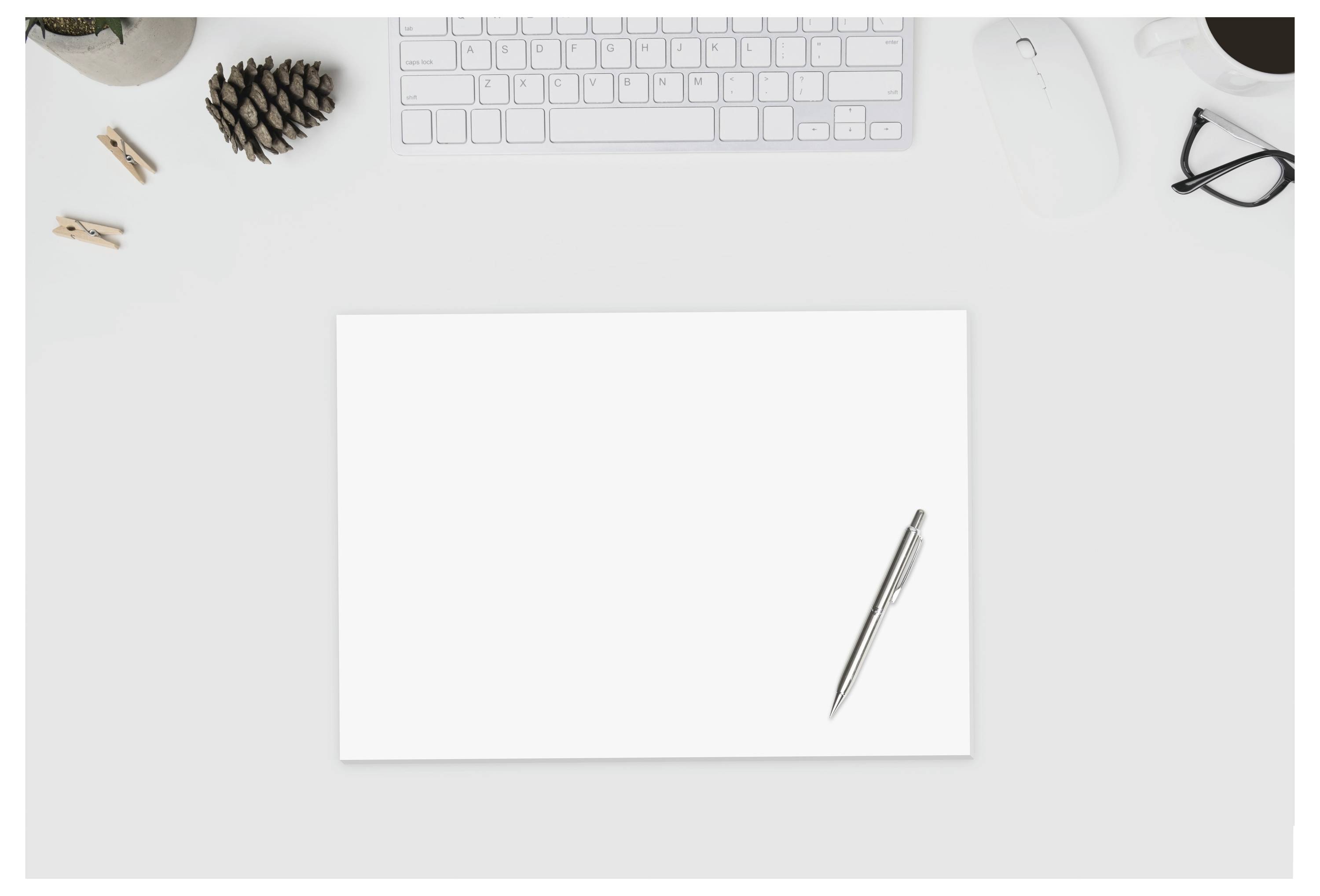 Leeres Blatt Papier auf einem aufgeräumten Schreibtisch mit einem Stift, einer Tastatur, einer Maus, einer Brille und kleinen Schreibtischutensilien