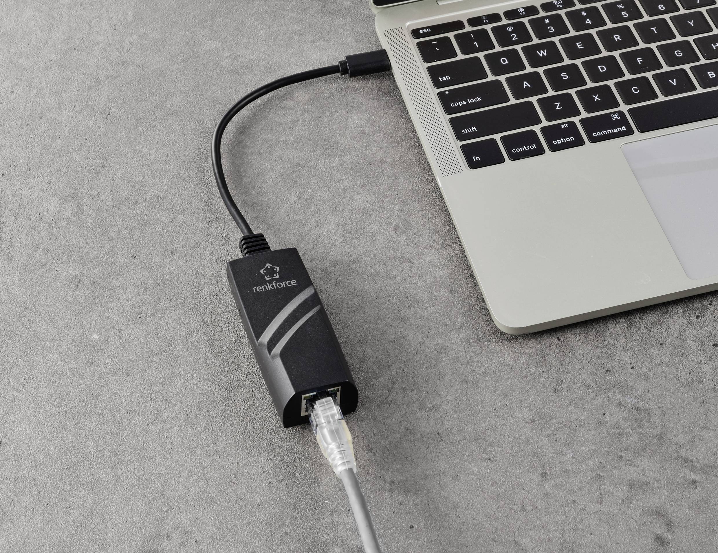 Ein Laptop ist mit einem Ethernet-Kabel über einen USB-Adapter verbunden, der auf einem grauen Tisch liegt.