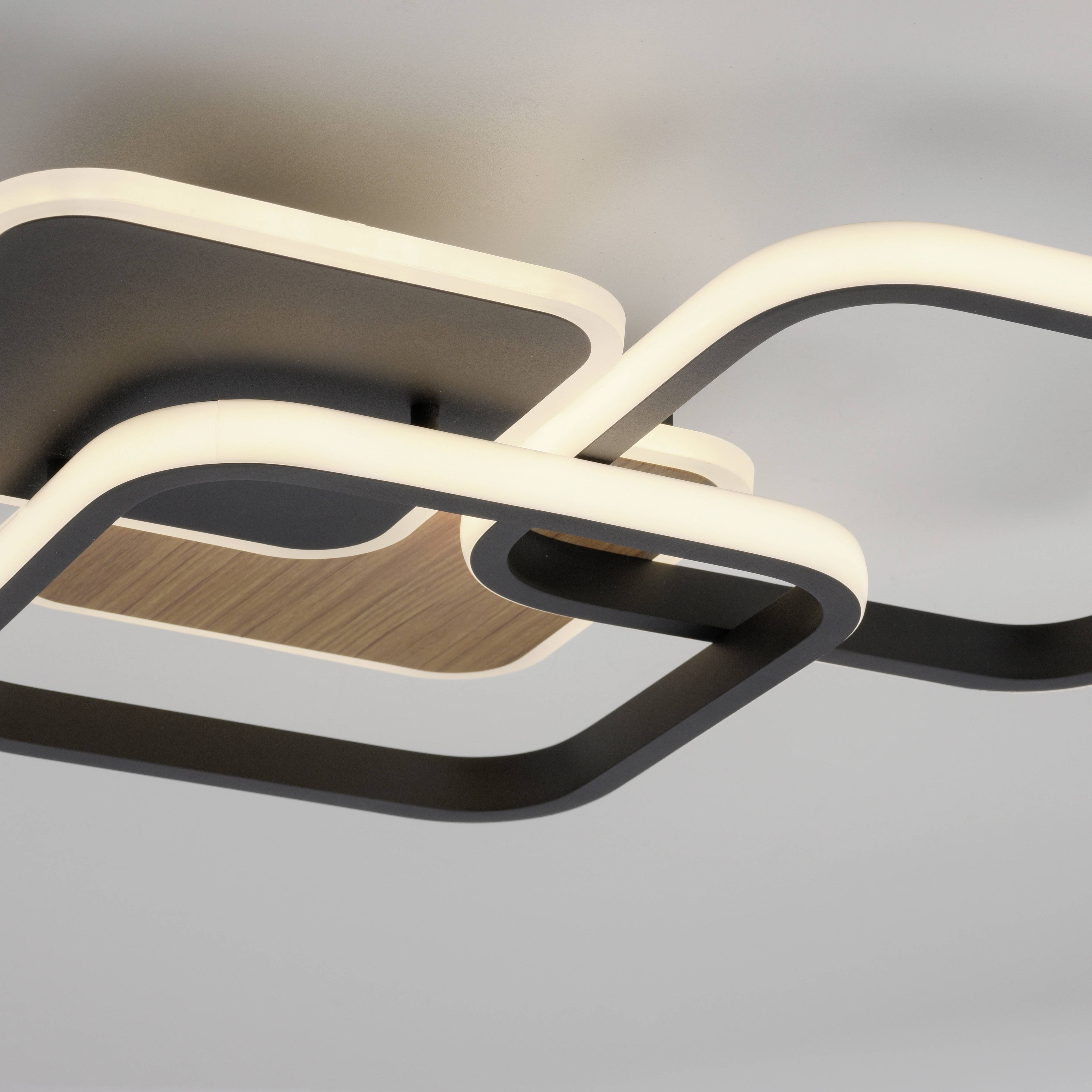 Moderne Deckenleuchte mit ineinander verschlungenen, rechteckigen LED-Rahmen in Schwarz und Holzoptik, montiert an einer weißen Decke.
