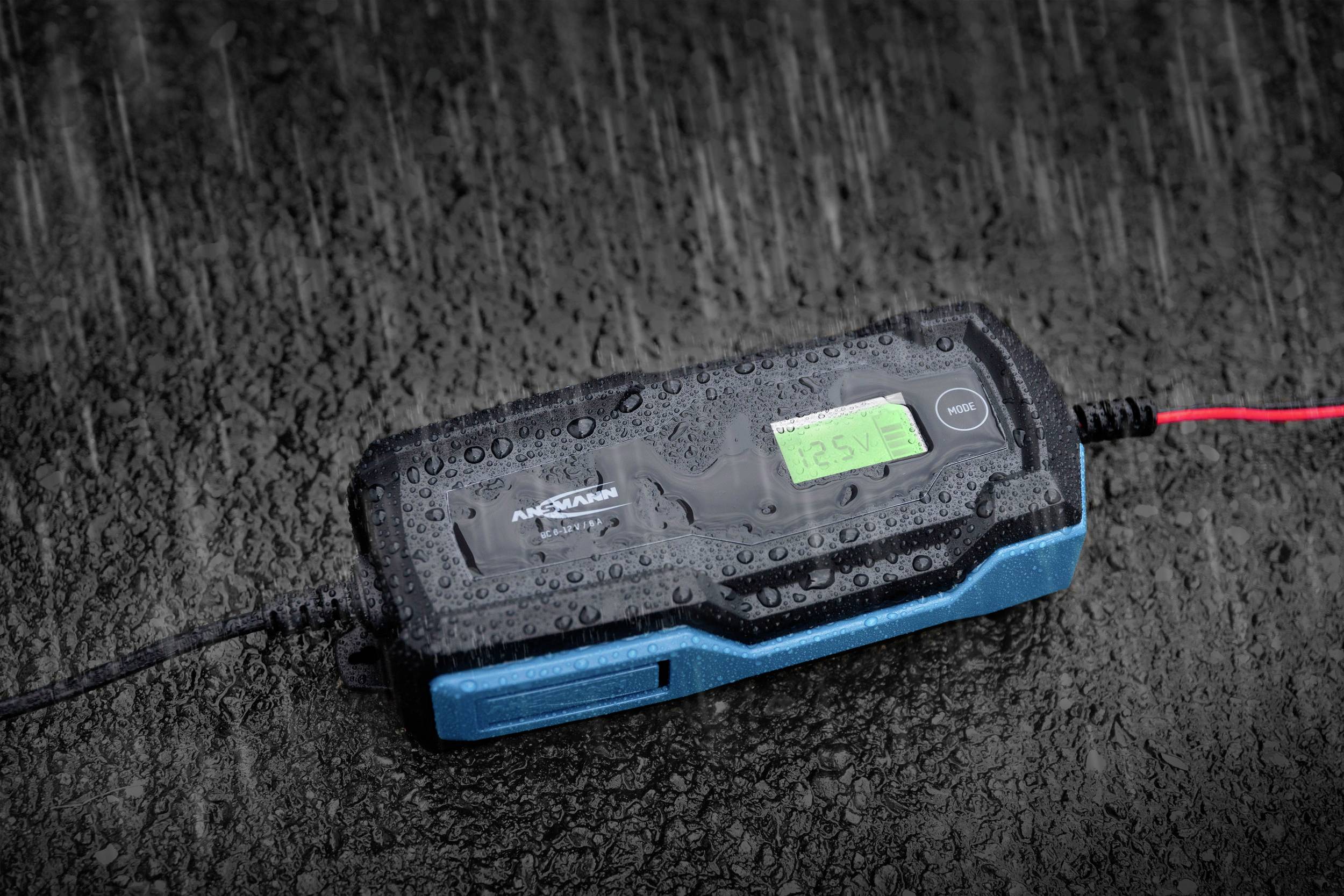 Ladegerät mit Regentropfen bedeckt, auf nasser Oberfläche liegend. Zeigt Wetterfestigkeit und Outdoor-Nutzung.