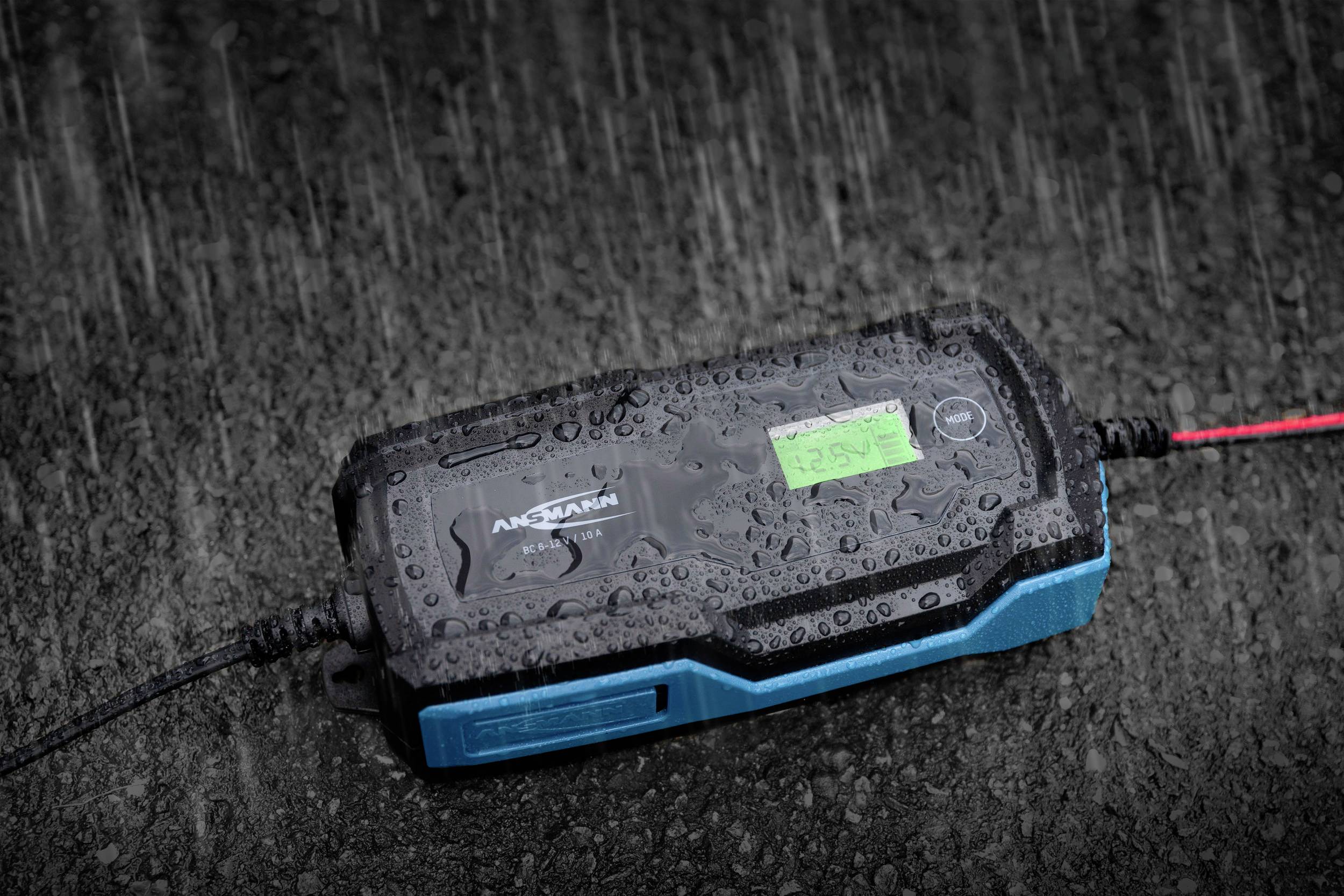 Ein batteriebetriebener Lader liegt auf nassem Asphalt unter starkem Regen.