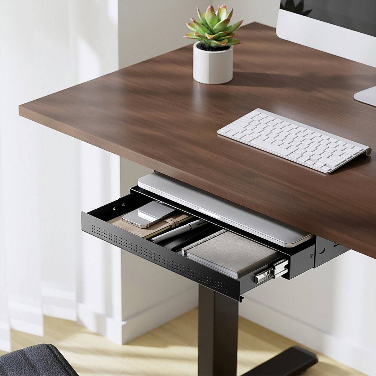 Schreibtisch mit Laptop, Tastatur und kleinem Blumentopf. Eine Schublade zeigt Dokumente und Notizbücher. Helliges Raumambiente.