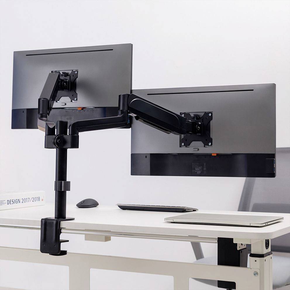 Zwei Monitore sind an einem Doppelmonitorhalterung an einem Schreibtisch montiert, was flexibles Arbeiten und ergonomische Positionierung ermöglicht.