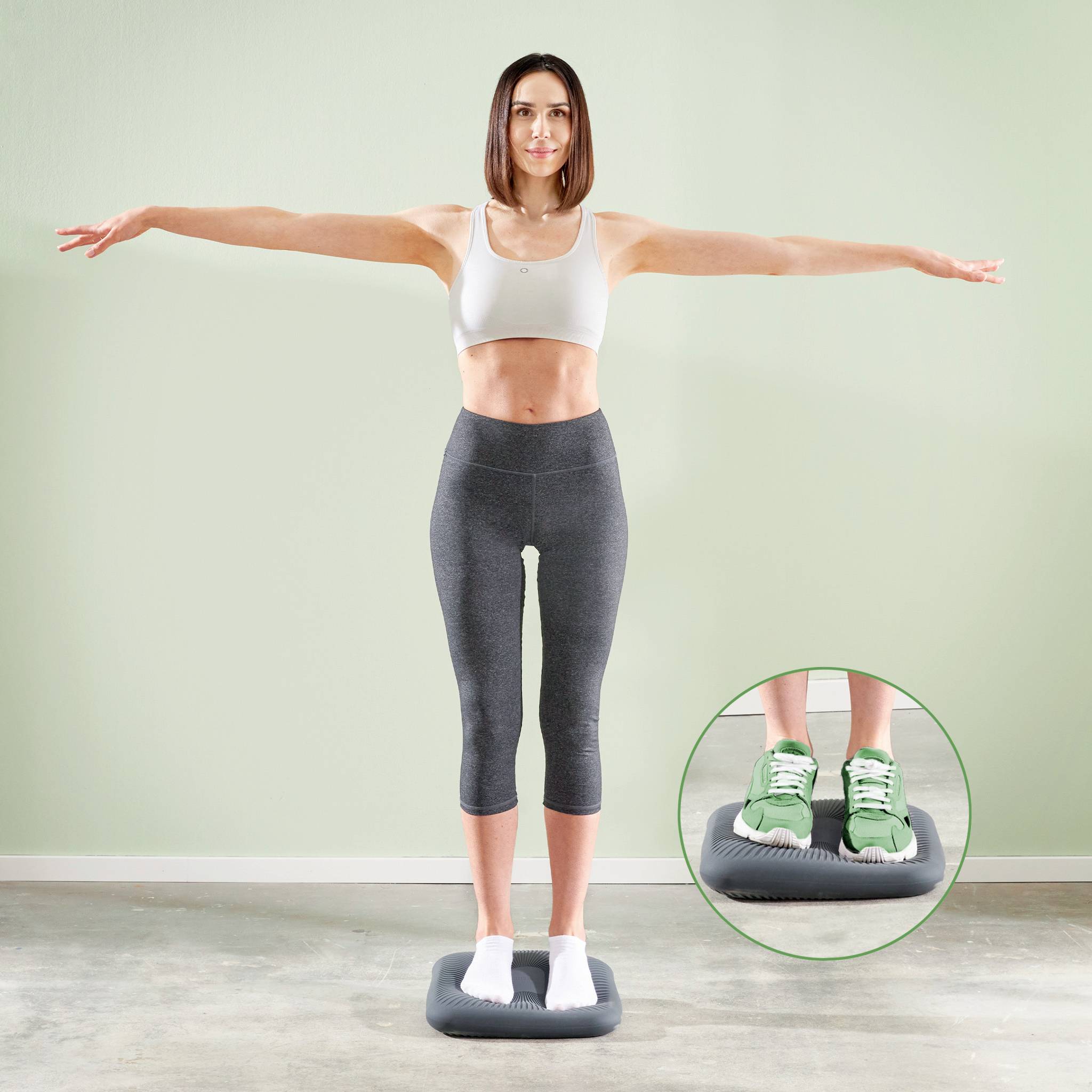 Eine Frau in Sportbekleidung balanciert auf einem Fitnessgerät, das an ihren Füßen vergrößert dargestellt ist, mit ausgestreckten Armen.