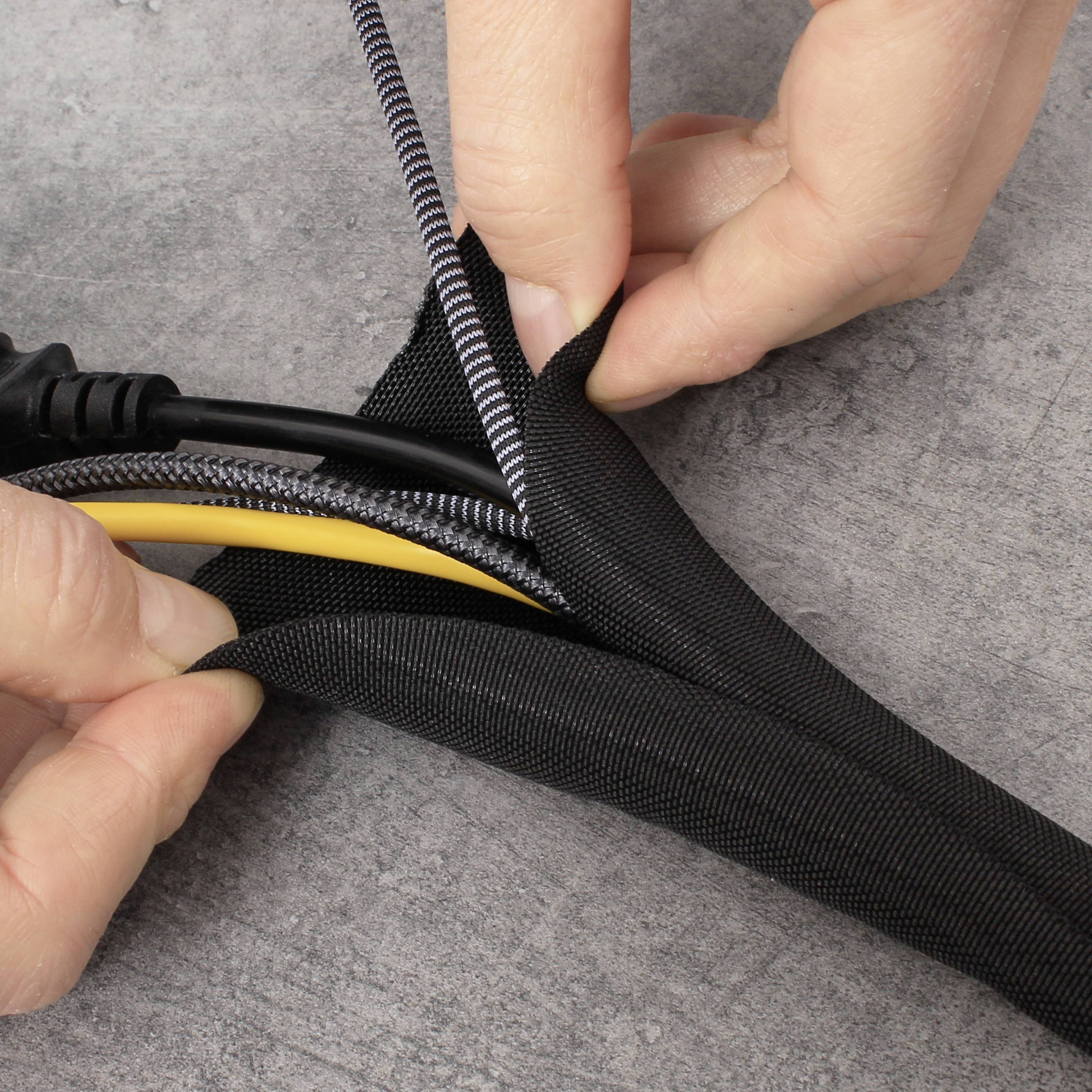 Eine Hand wickelt Kabel in einen schwarzen Kabelschlauch auf einem grauen Hintergrund.
