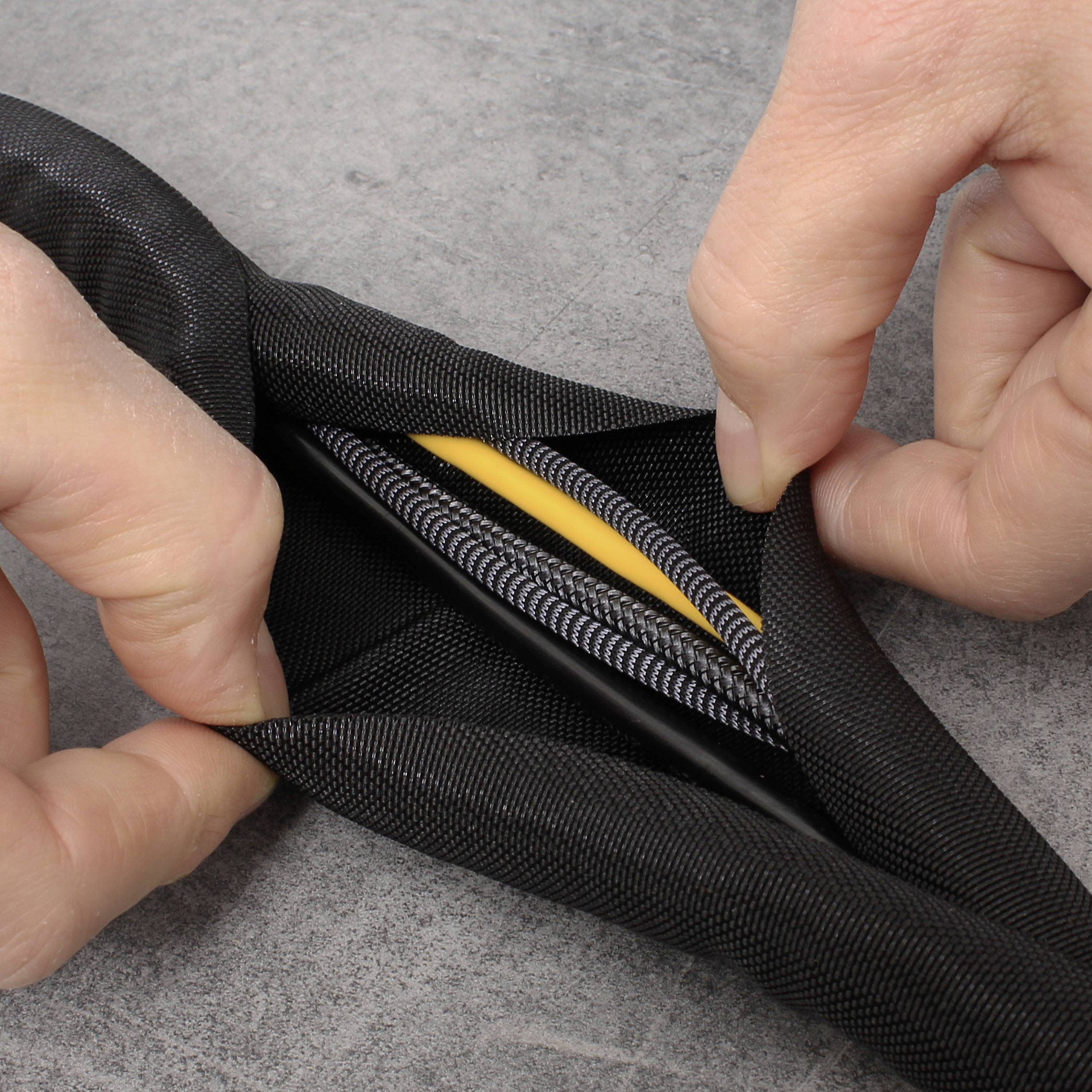 Zwei Hände halten ein geflochtenes Kabelmanagement, das verschiedene bunte Kabel umschließt, auf einem grauen Untergrund.