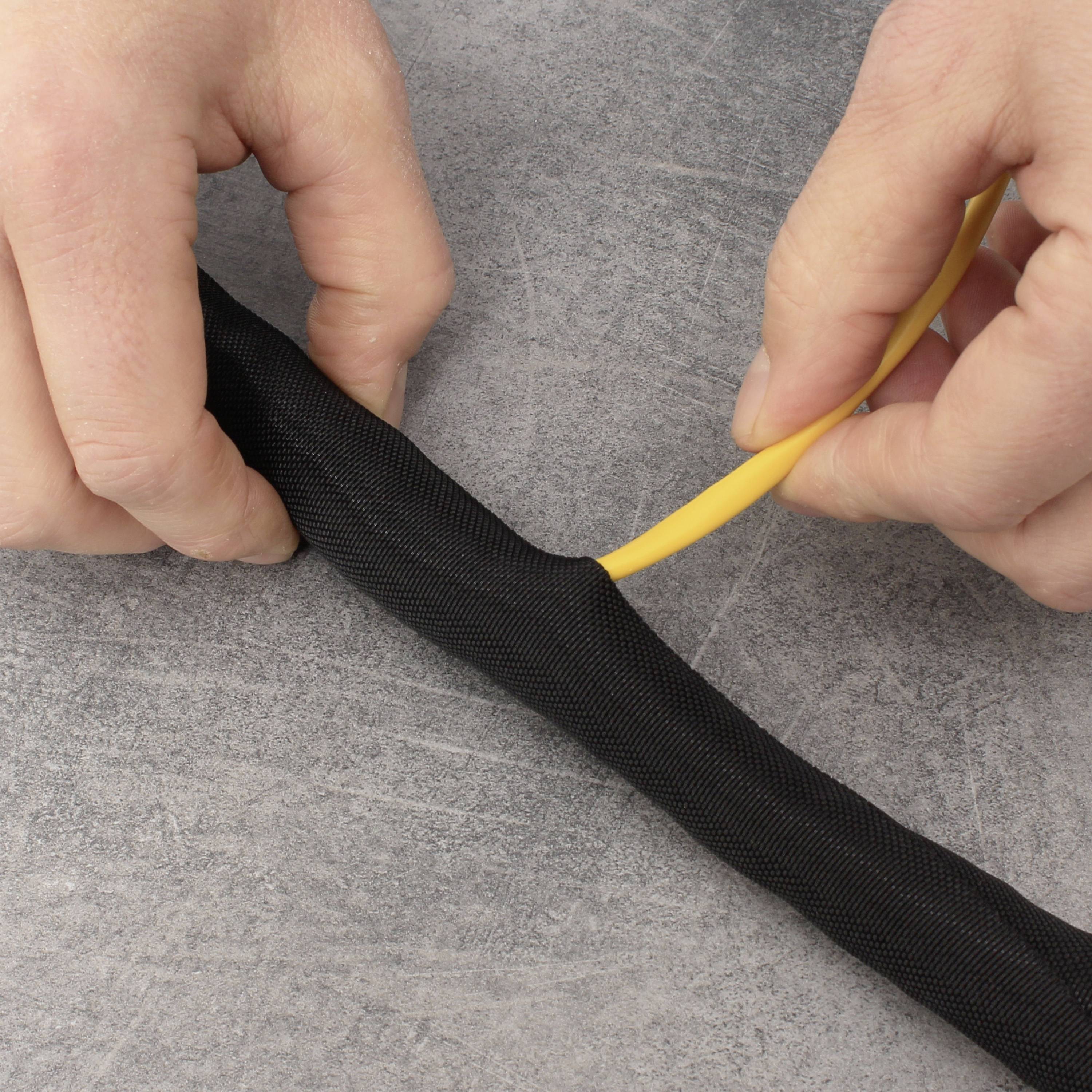 Eine Person zieht ein gelbes Kabel in einen schwarzen Kabelschutz ein, um das Kabel zu sichern und zu schützen.
