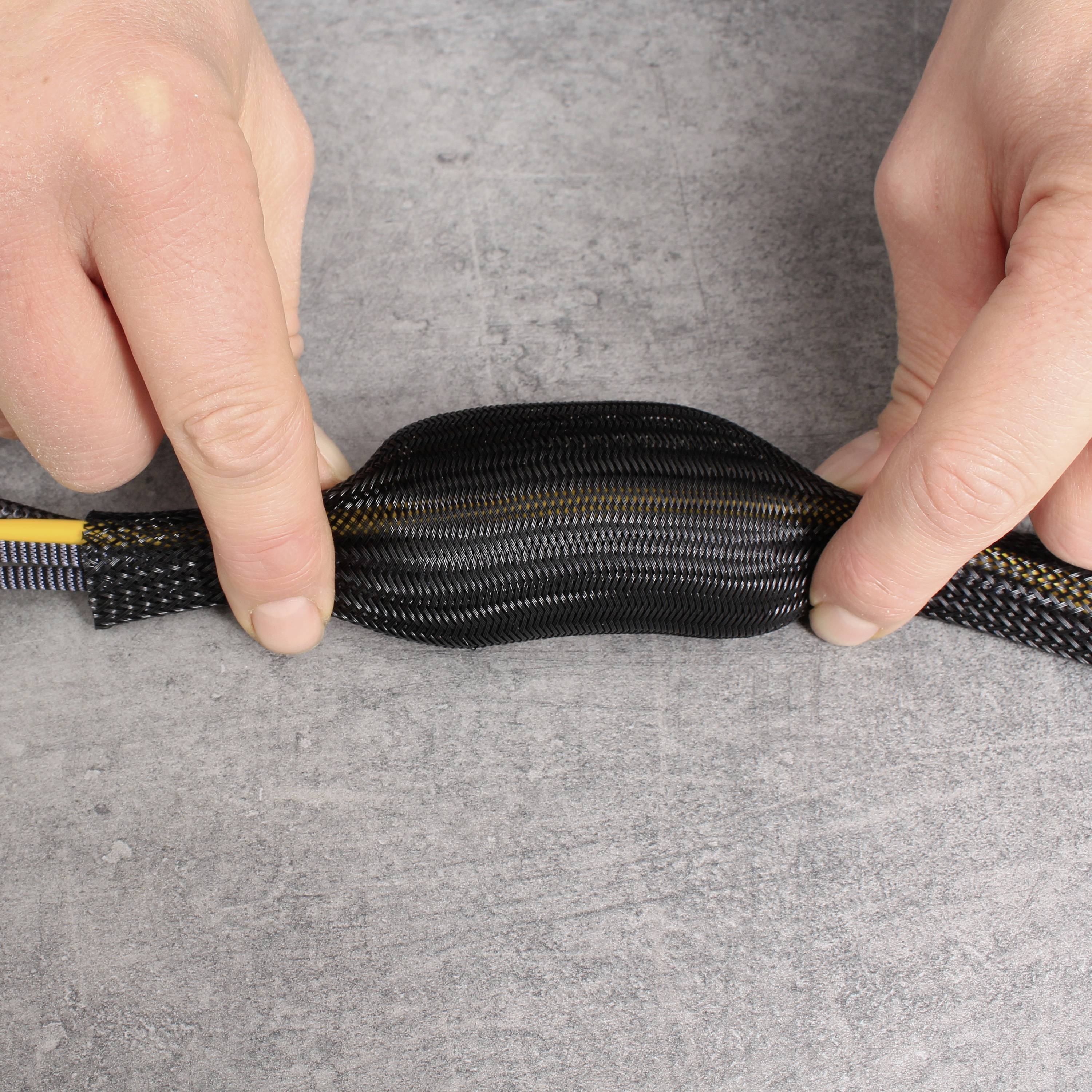 Zwei Hände halten ein schwarzes Kabelsleeve, das mehrere bunte Kabel umhüllt. Das Sleeve schützt und bündelt die Kabel auf einem grauen Hintergrund.