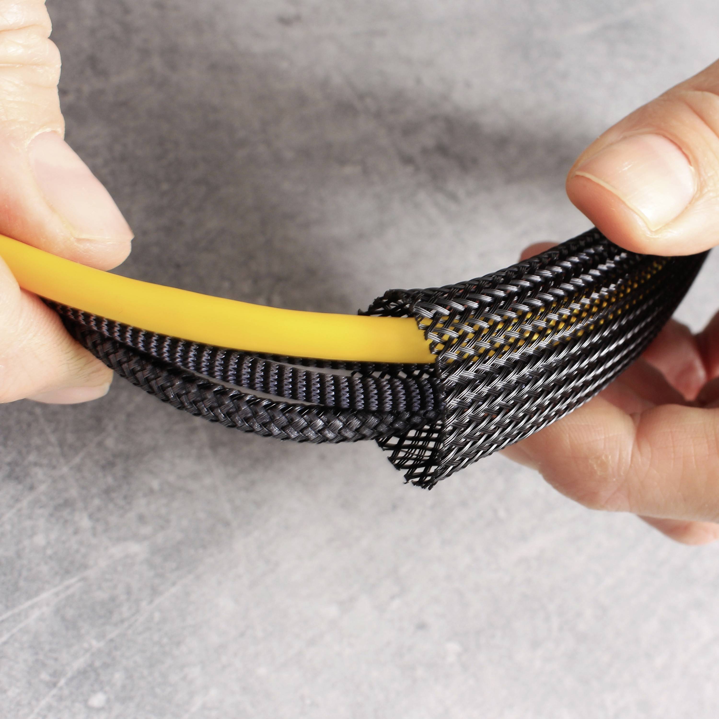 Eine Hand hält ein flexibles, geflochtenes Kabelschutzrohr, das ein gelbes Kabel umhüllt und vor Beschädigung schützt.