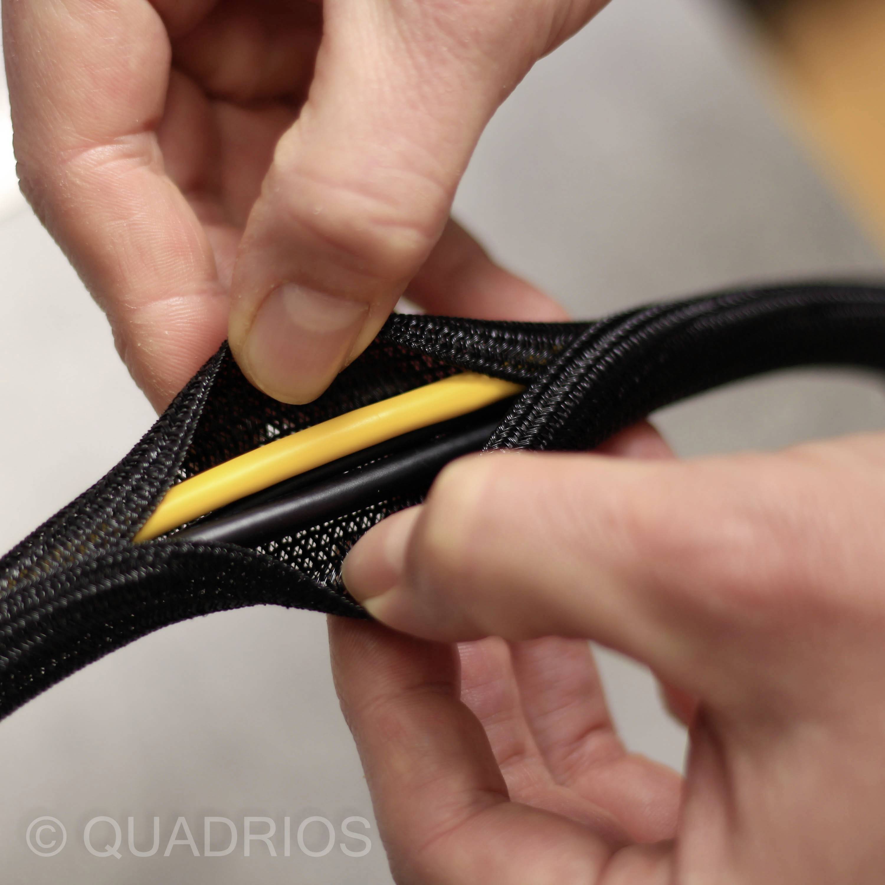 Hände ziehen ein schwarzes Kabelmanagement mit gelbem und schwarzem Kabel auseinander.