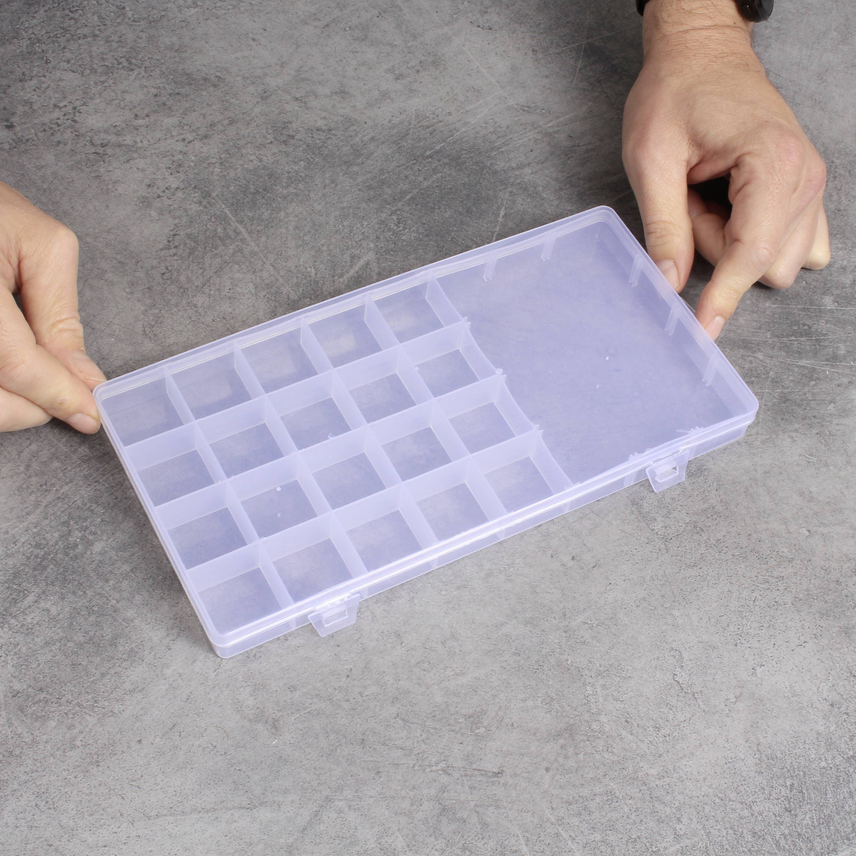 Person hält eine transparente Kunststoffbox mit mehreren kleinen Fächern, geeignet zur Aufbewahrung von Kleinteilen.
