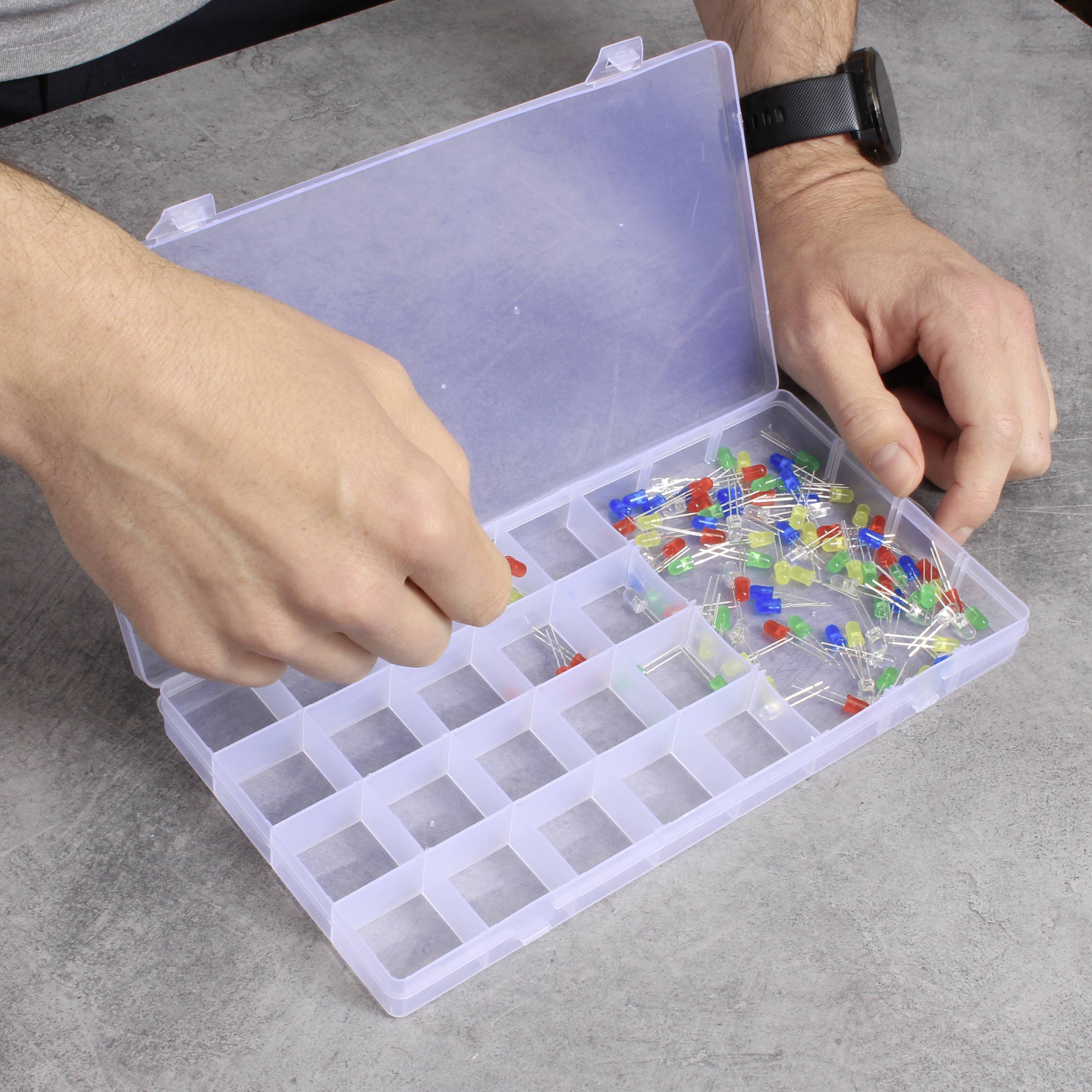 Eine Person sortiert bunte Stecknadeln in einem Plastikorganizer mit Fächern auf einem grauen Tisch.