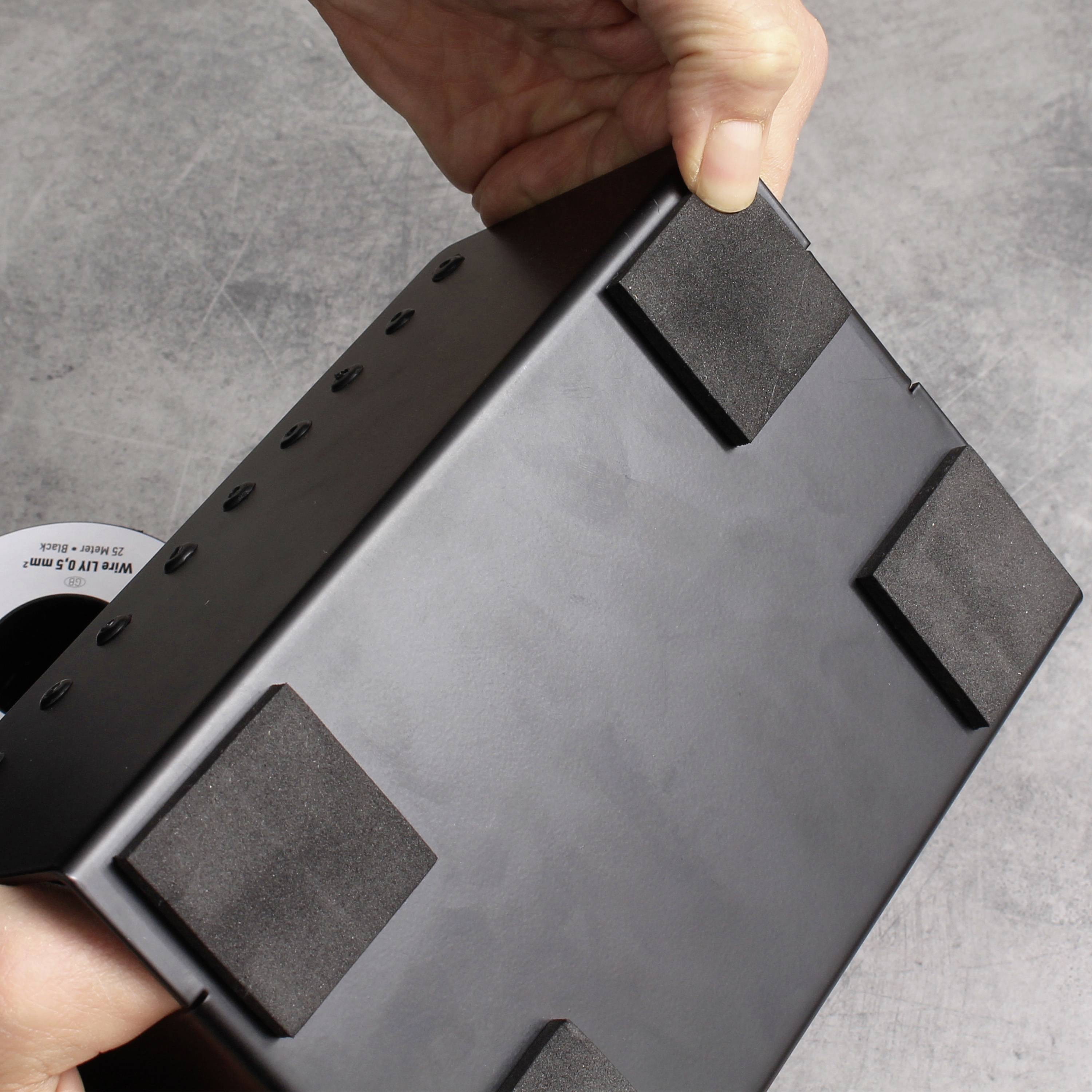 Eine Hand hält eine schwarze elektronische Waage von unten. Vier rutschfeste Polster sind auf der Unterseite der Waage zu sehen.