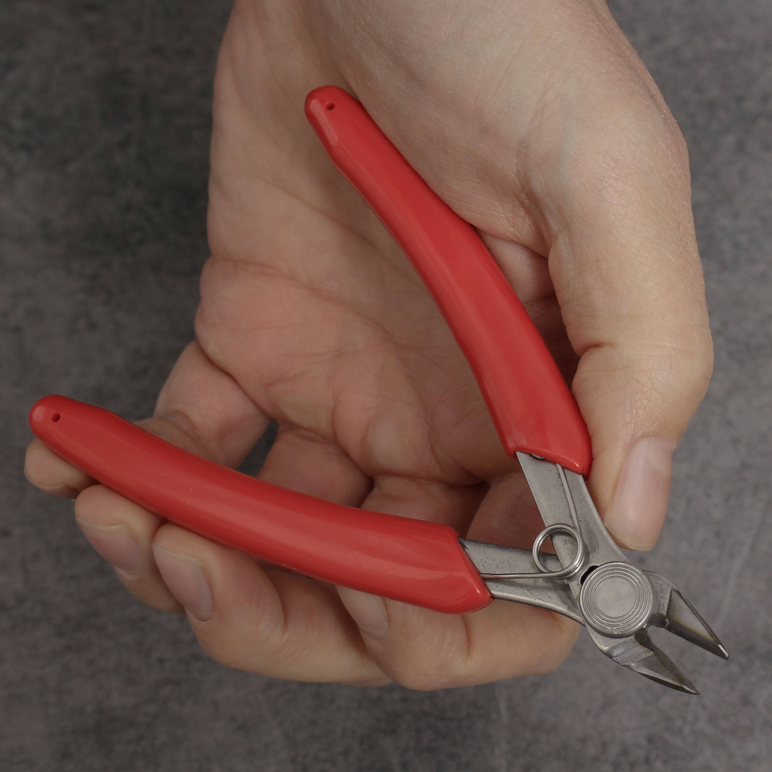 Eine Hand hält eine Drahtschere mit roten Griffen.