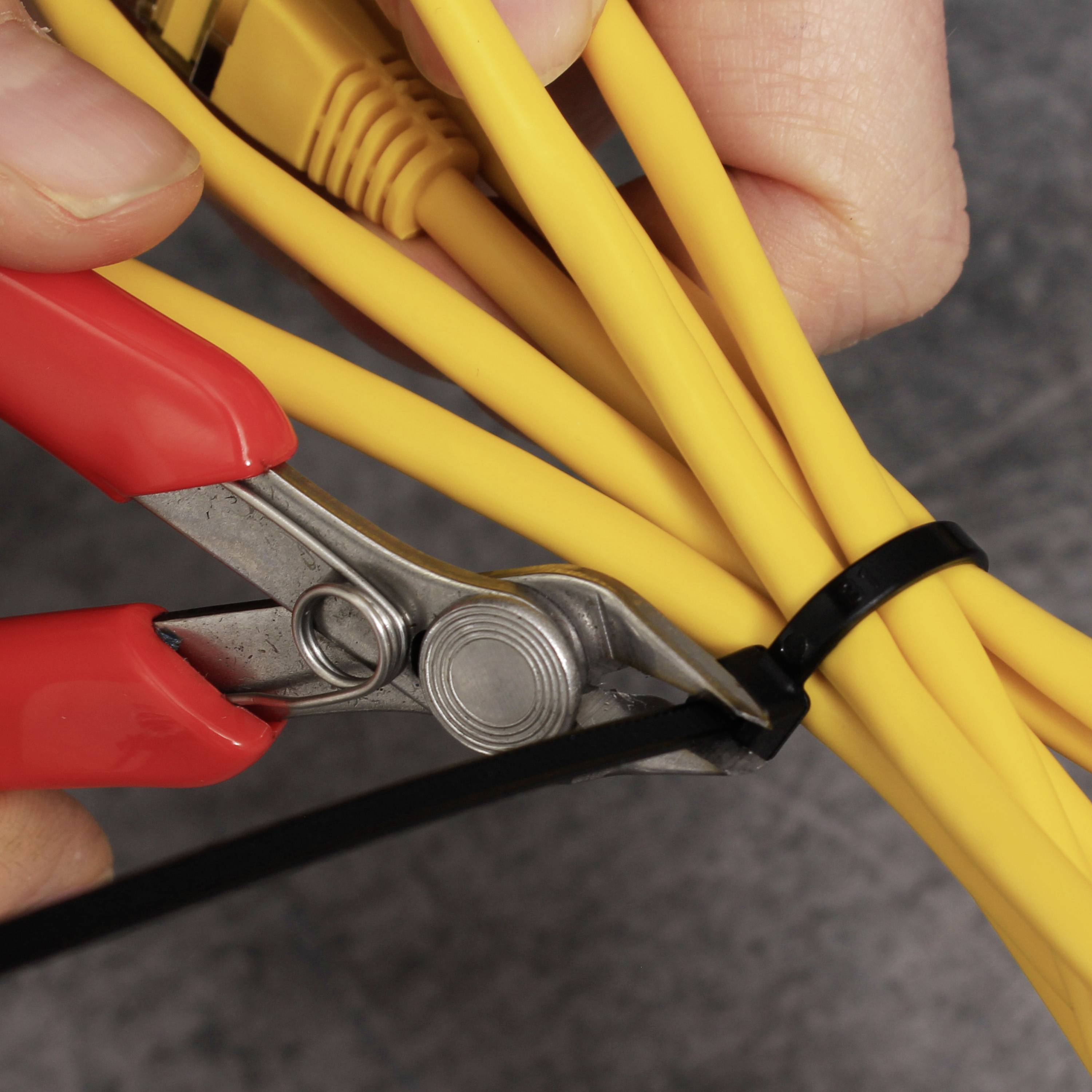 Eine Hand hält eine Zange und schneidet ein schwarzes Kabelbinder, der gelbe Kabel zusammenhält.