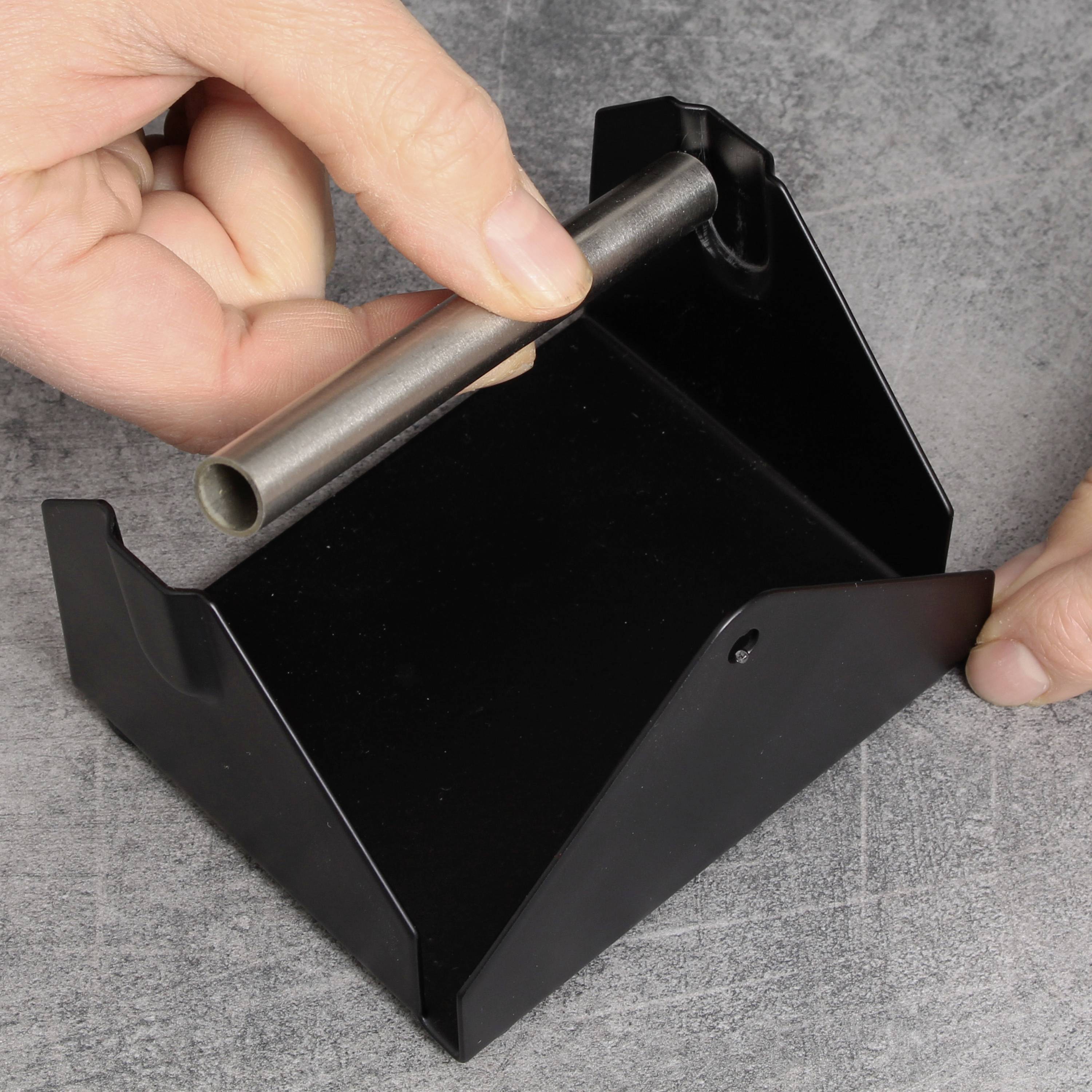 Zwei Hände montieren ein Metallrohr in eine schwarze Halterung auf einem grauen Untergrund.