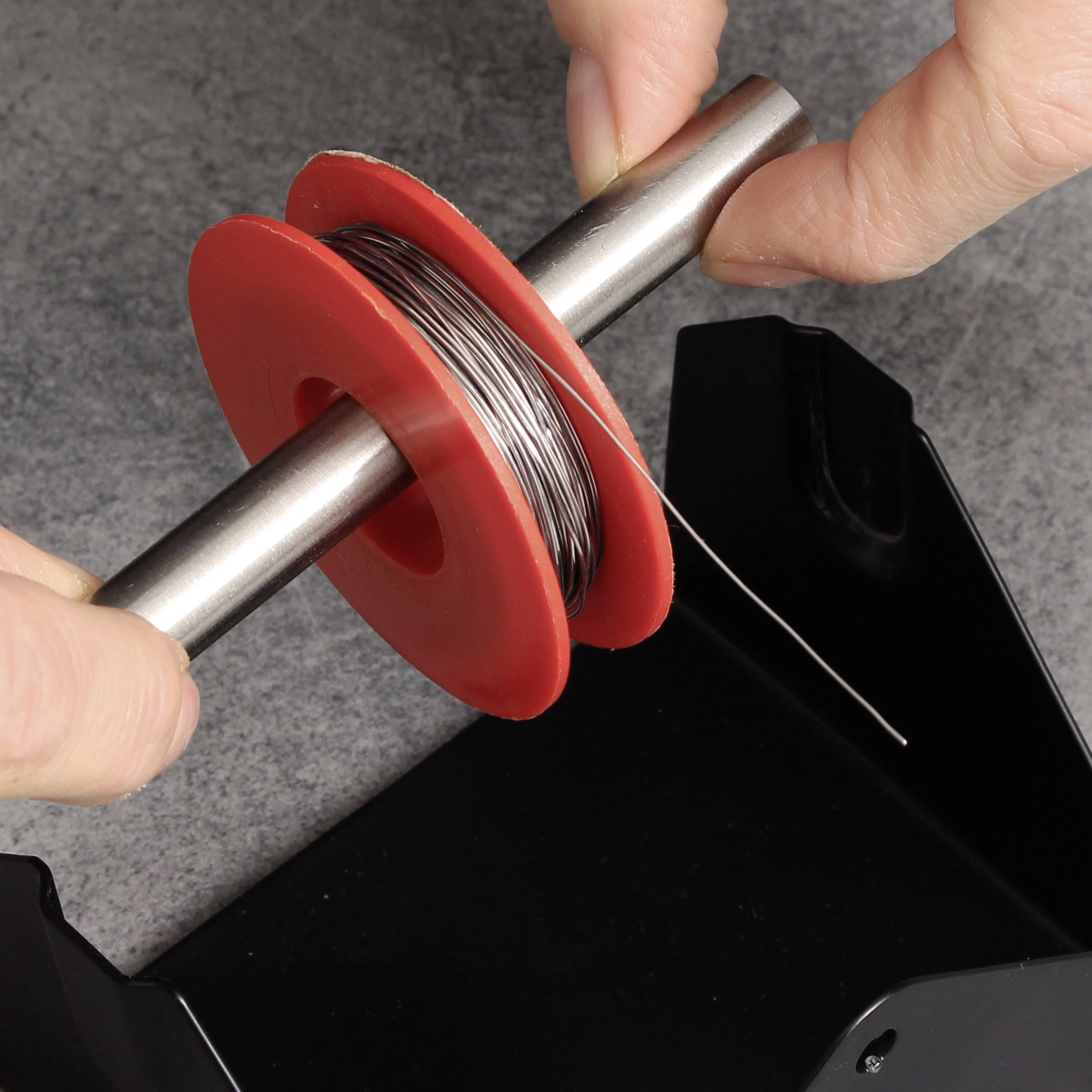 Eine Person hält eine rote Spule, die mit dünnem Metallkabel umwickelt ist, zwischen den Händen.