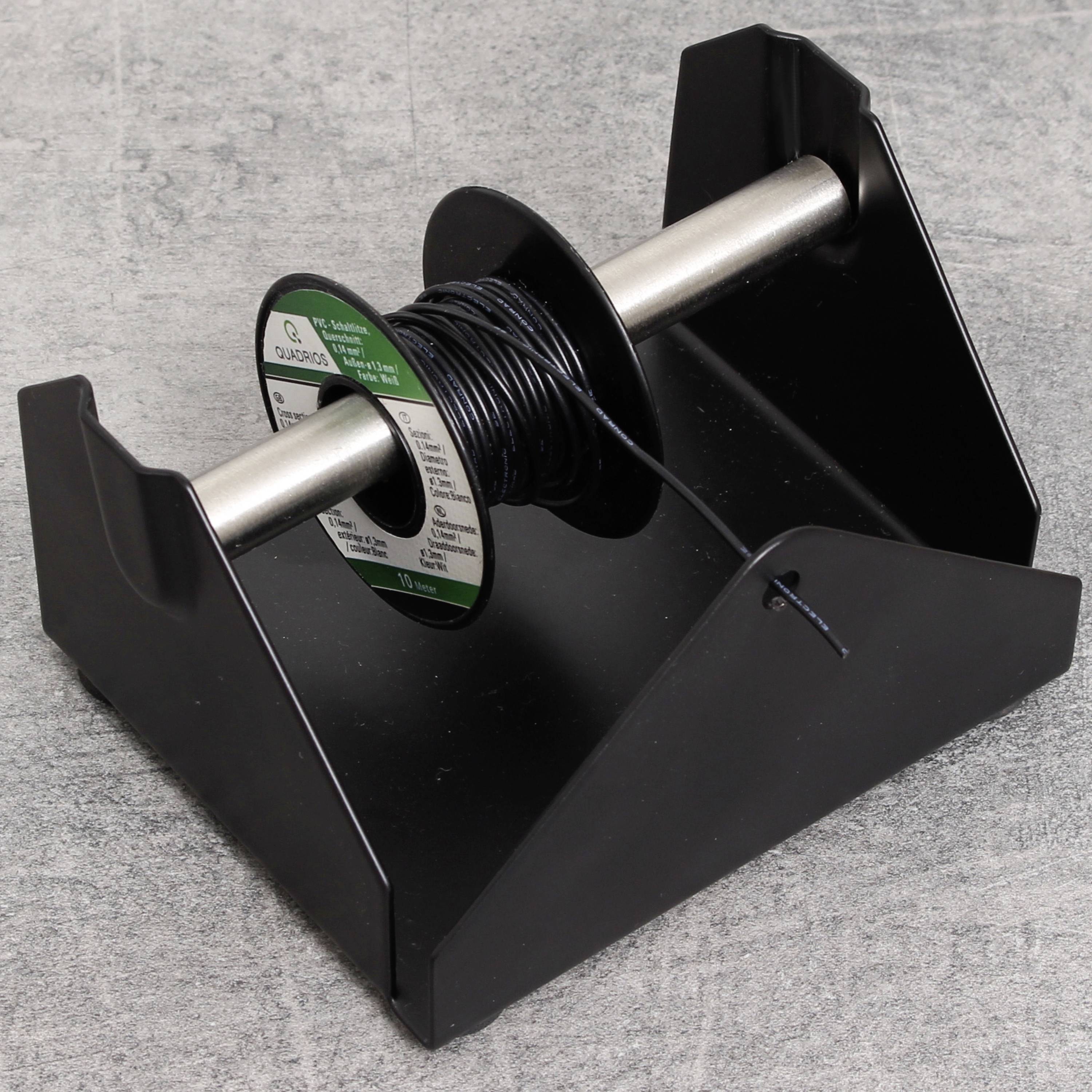 Eine Spule mit schwarzem Draht liegt auf einem schwarzen Halter aus Metall. Der Boden ist grau.