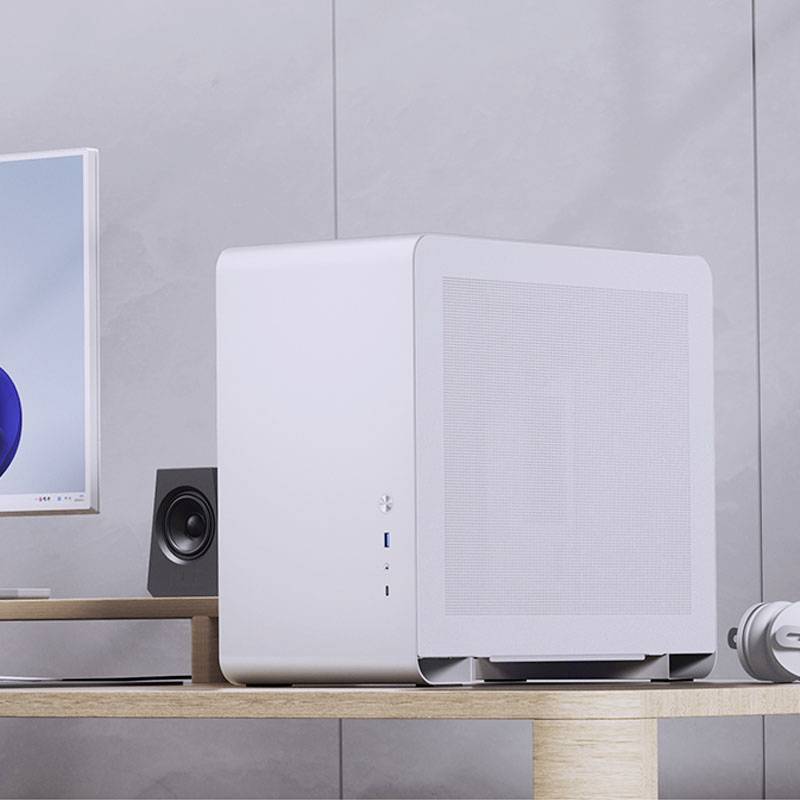 Ein minimalistischer Computer auf einem Holztisch, neben einem Bildschirm und Lautsprechern, deutet auf eine moderne Arbeitsumgebung hin.