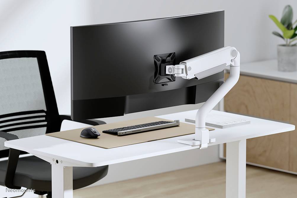 Ein moderner Schreibtisch mit gebogenem Monitor, Tastatur und Maus. Im Hintergrund befindet sich ein weißer Aktenschrank und eine Topfpflanze.