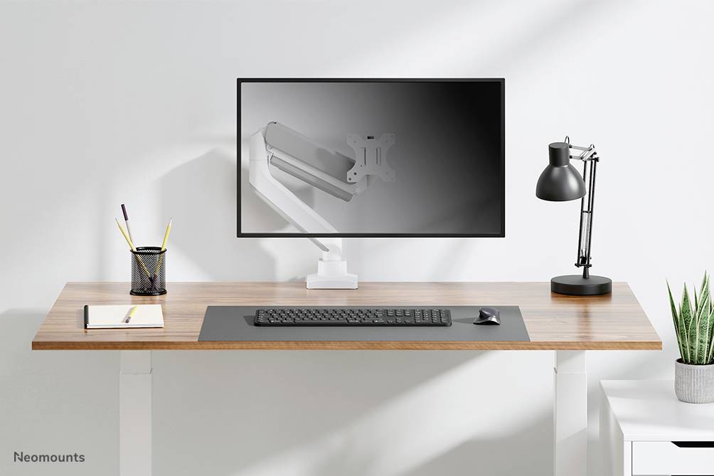 Moderner Schreibtisch mit Bildschirm und Lampe, Tastatur, Notizbuch und Stiftehalter. Der Bildschirm zeigt ein Bild eines Monitorarms.