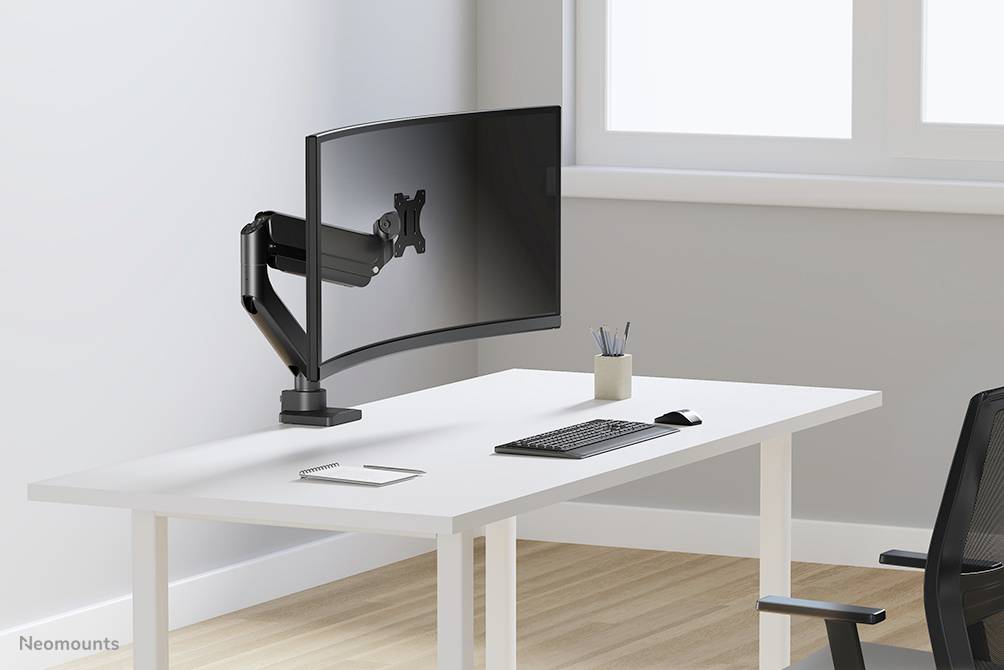 Ein leerer Schreibtisch mit gebogenem Monitorhalterungsarm, Tastatur und Maus; Fenster im Hintergrund.