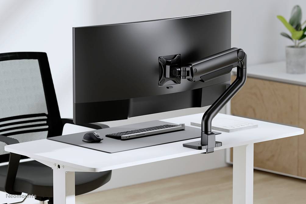 Ein moderner Arbeitsplatz mit einem gebogenen Monitor auf einem Schwenkarm, einer Tastatur, einer Maus auf einem weißen Tisch. Ein Bürostuhl steht daneben.