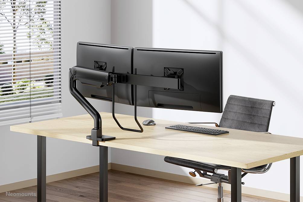 Ein Schreibtisch mit zwei an einem Monitorarm montierten Bildschirmen, einer Tastatur und einer Maus. Ein Stuhl steht daneben.