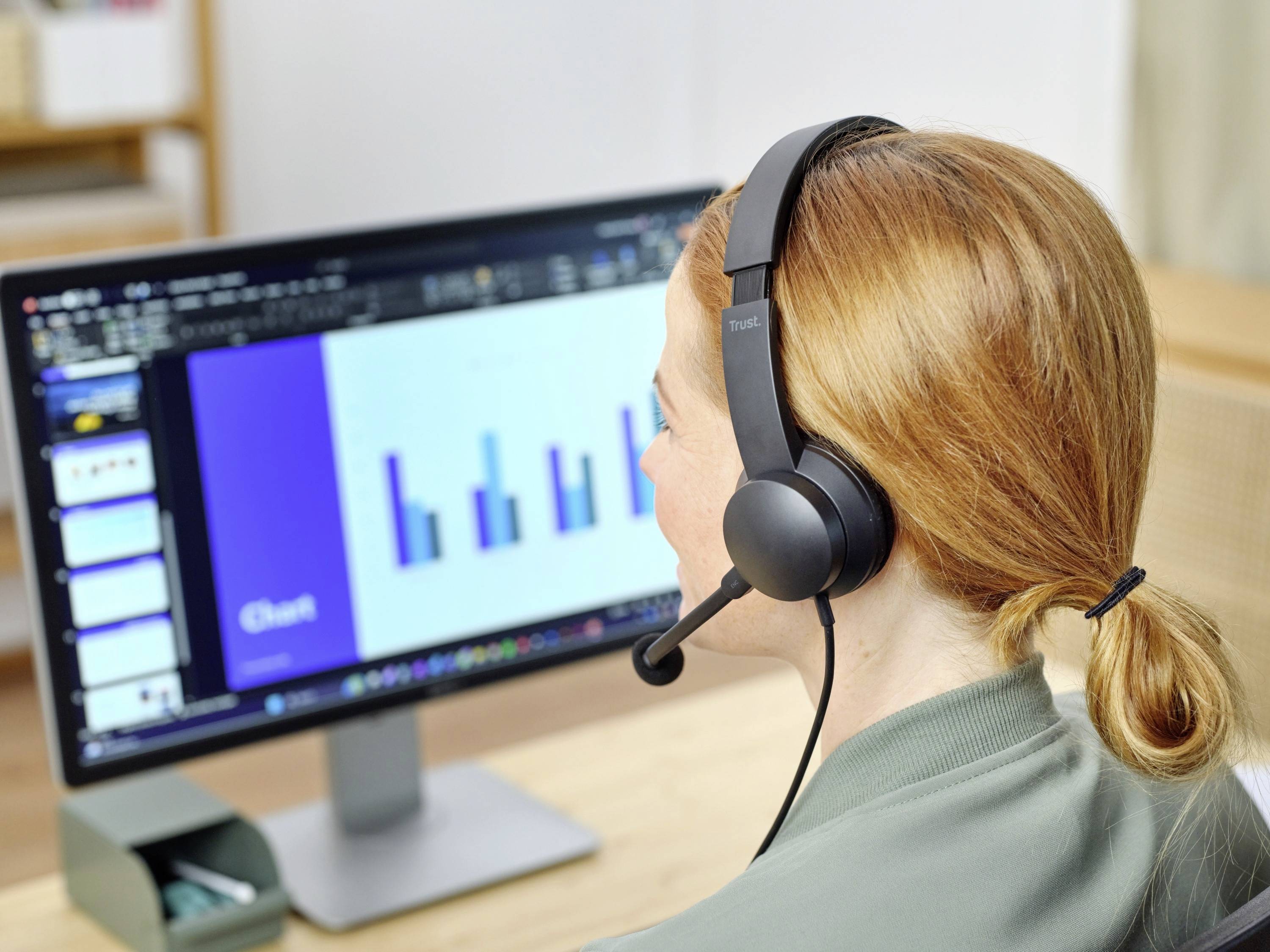 Person mit Headset betrachtet Computerbildschirm mit Präsentation und Diagrammen.