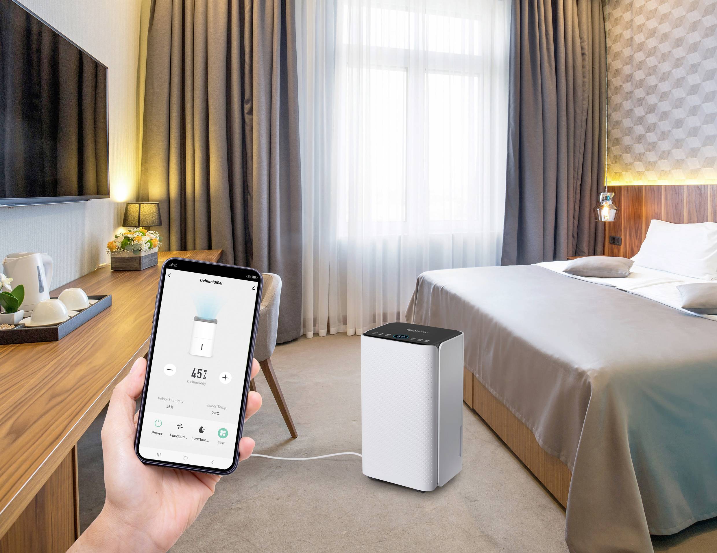 Ein Hotelzimmer mit einem Bett und einem Luftreiniger auf dem Boden. Eine Hand hält ein Smartphone, das die Steuerung des Luftreinigers zeigt.