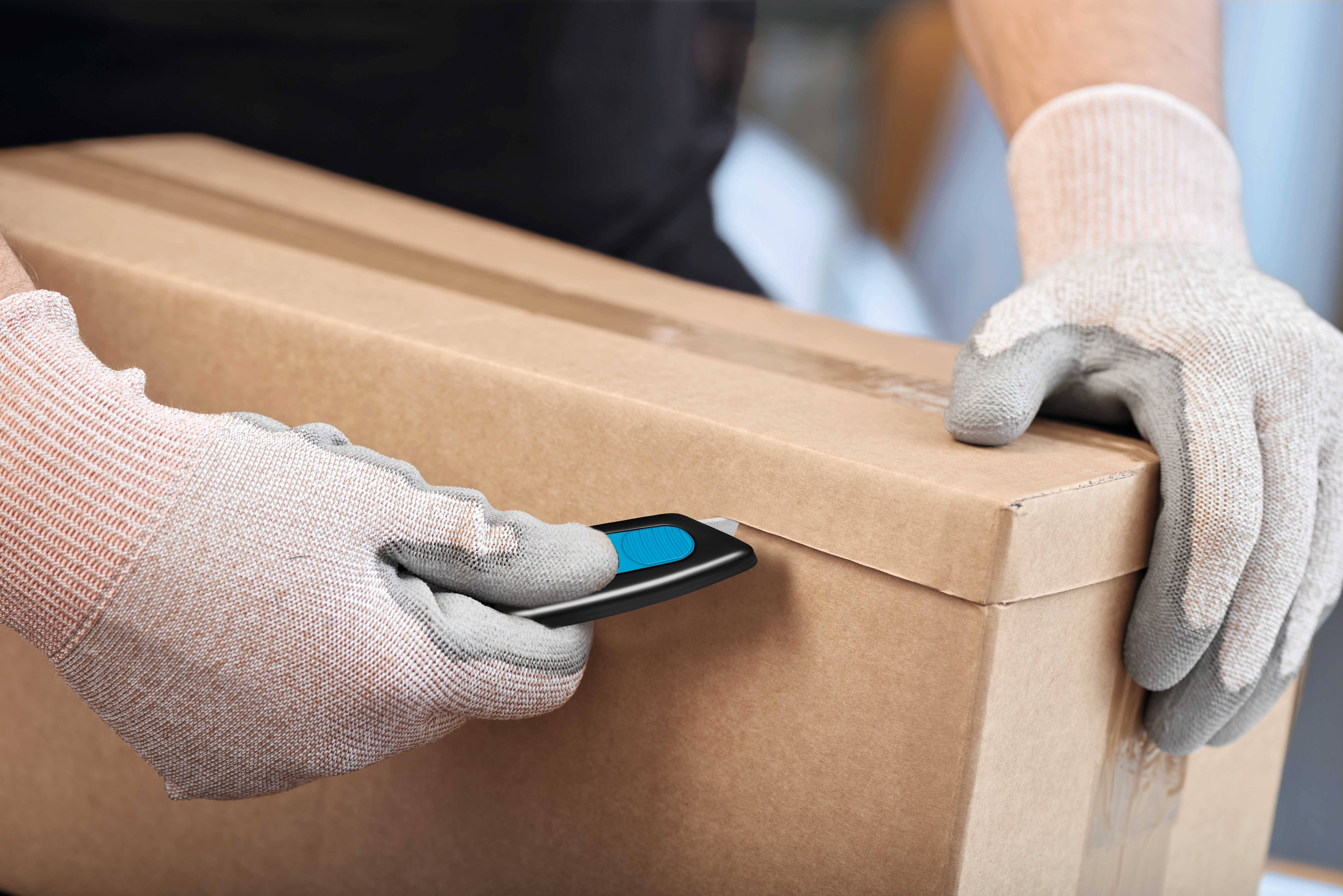 Eine Person mit Handschuhen öffnet einen Karton mit einem Cutter.