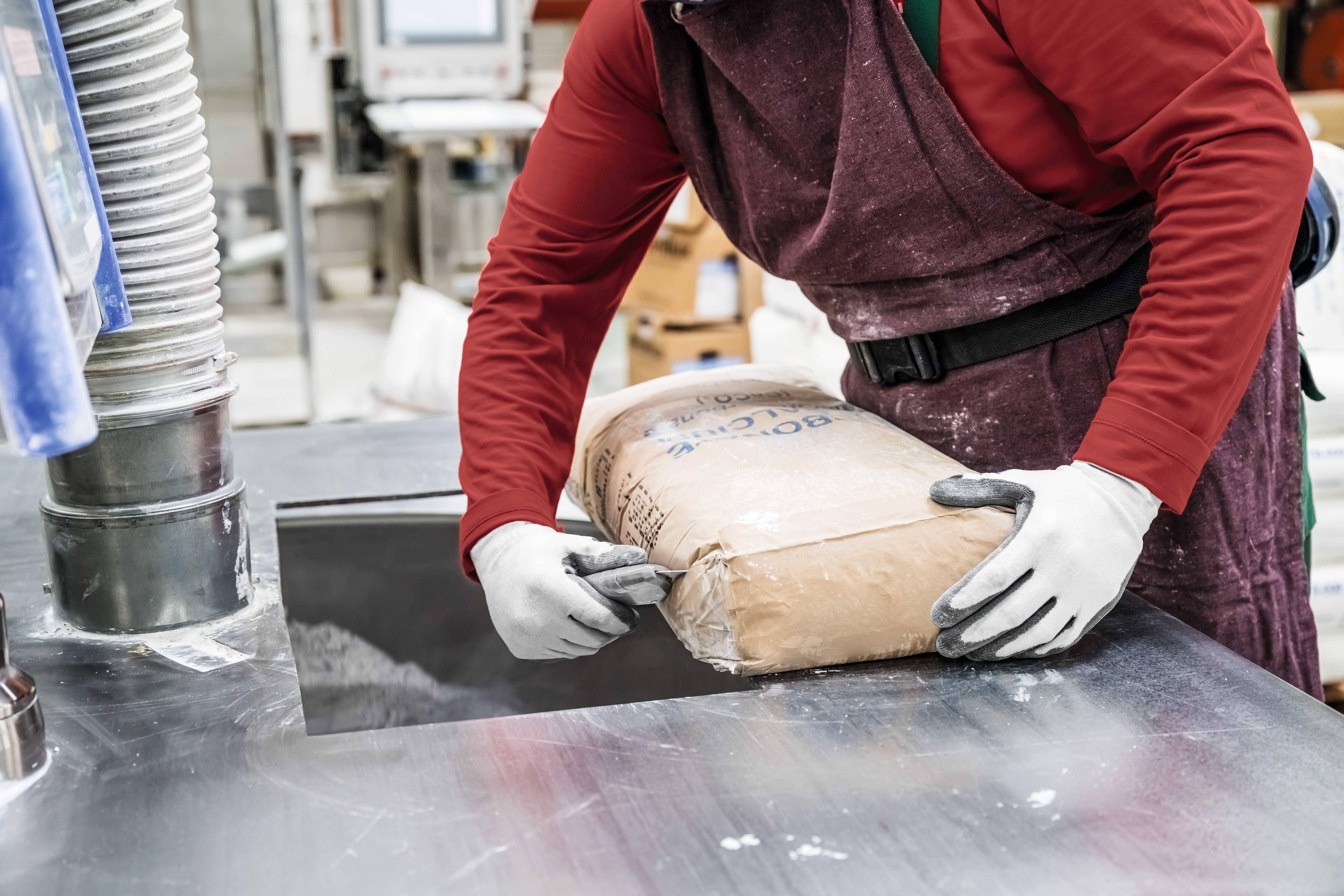 Eine Person in Arbeitskleidung kippt einen Sack Mehl in eine Maschine in einer Lebensmittelverarbeitungsanlage.