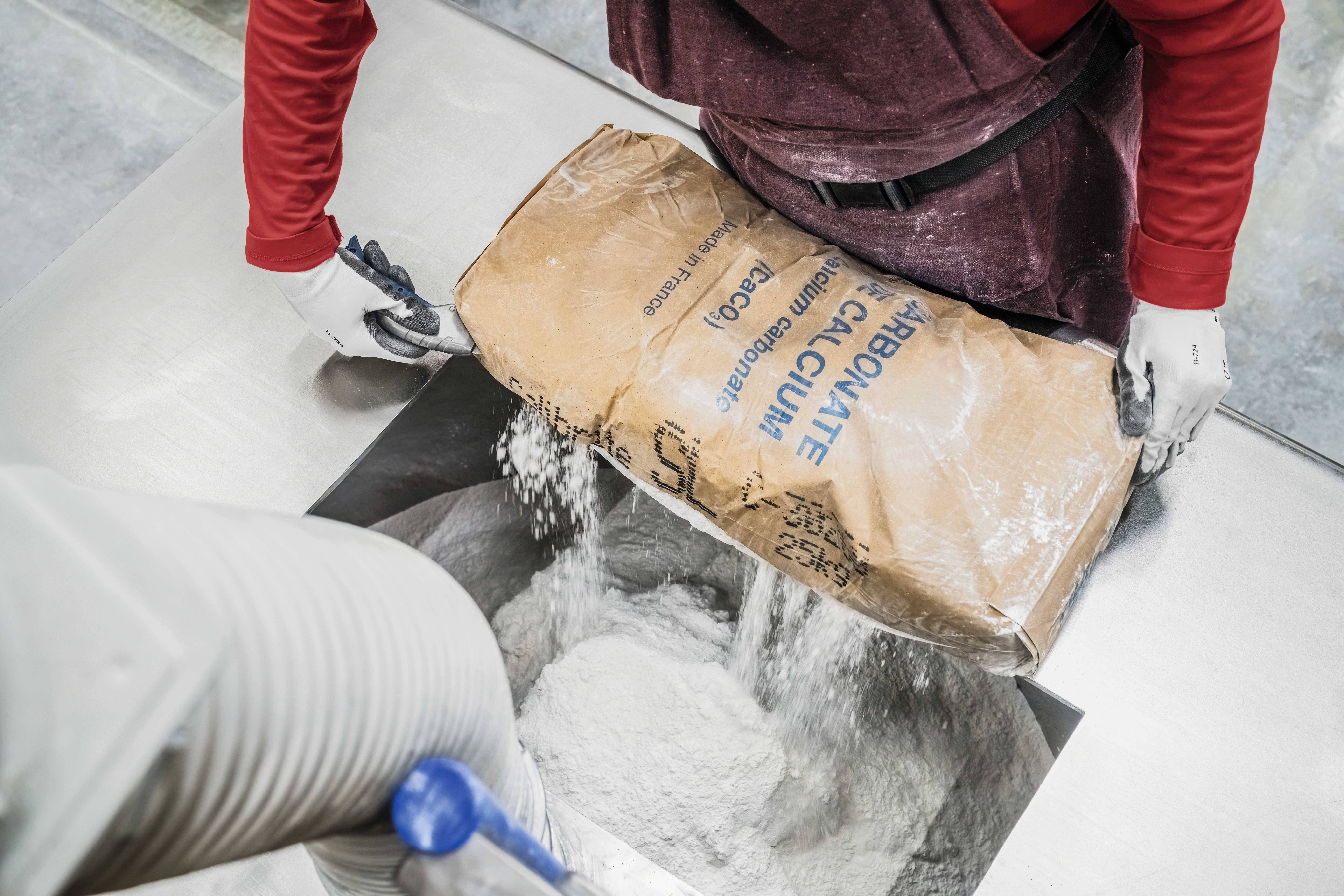 Person gießt weißen Pulverbeutel in eine Maschine.