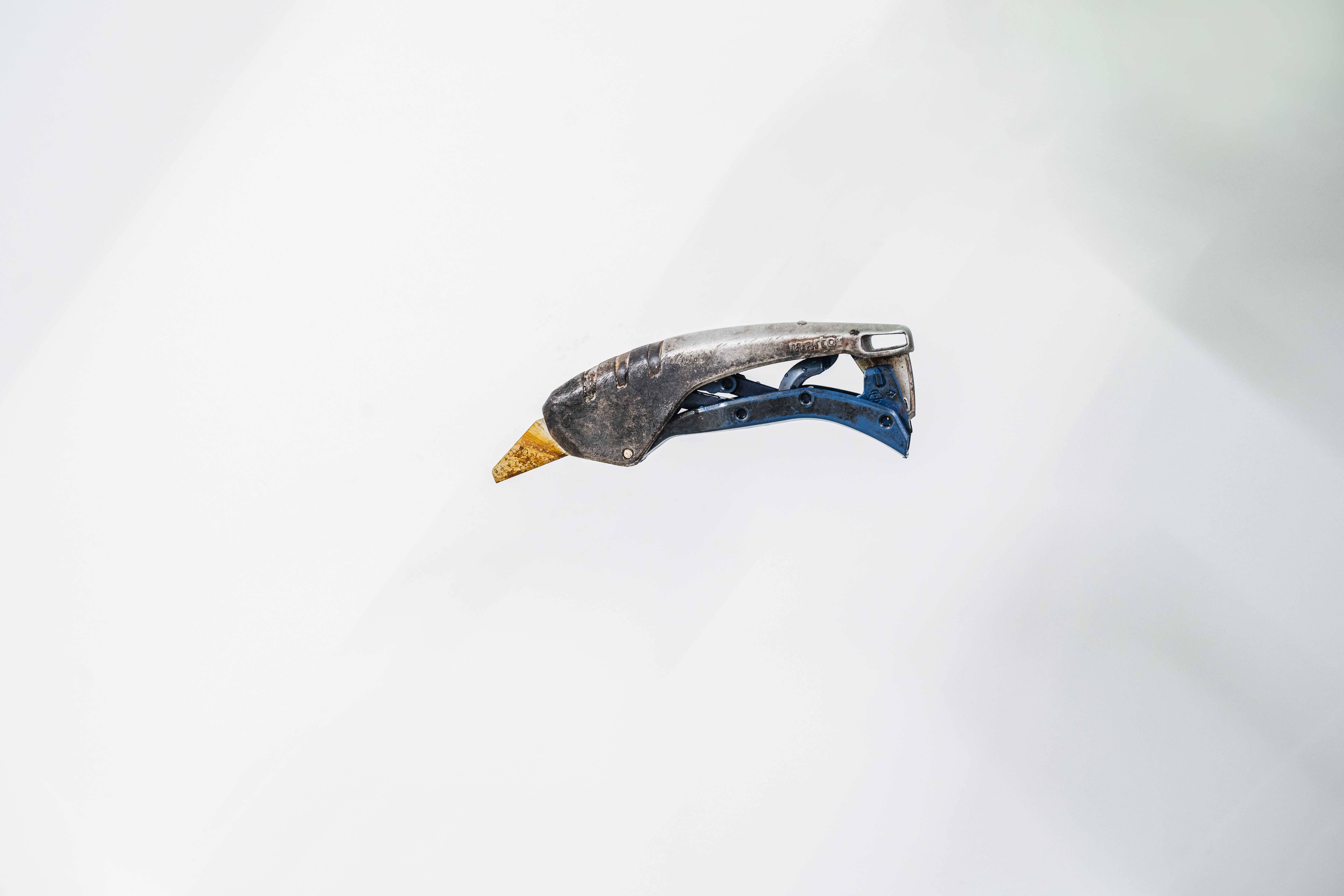 Ein altes, leicht angerostetes Werkzeug mit einem blauen Griff liegt vor einem weißen Hintergrund. Wahrscheinlich ein Griff eines Gartengeräts.