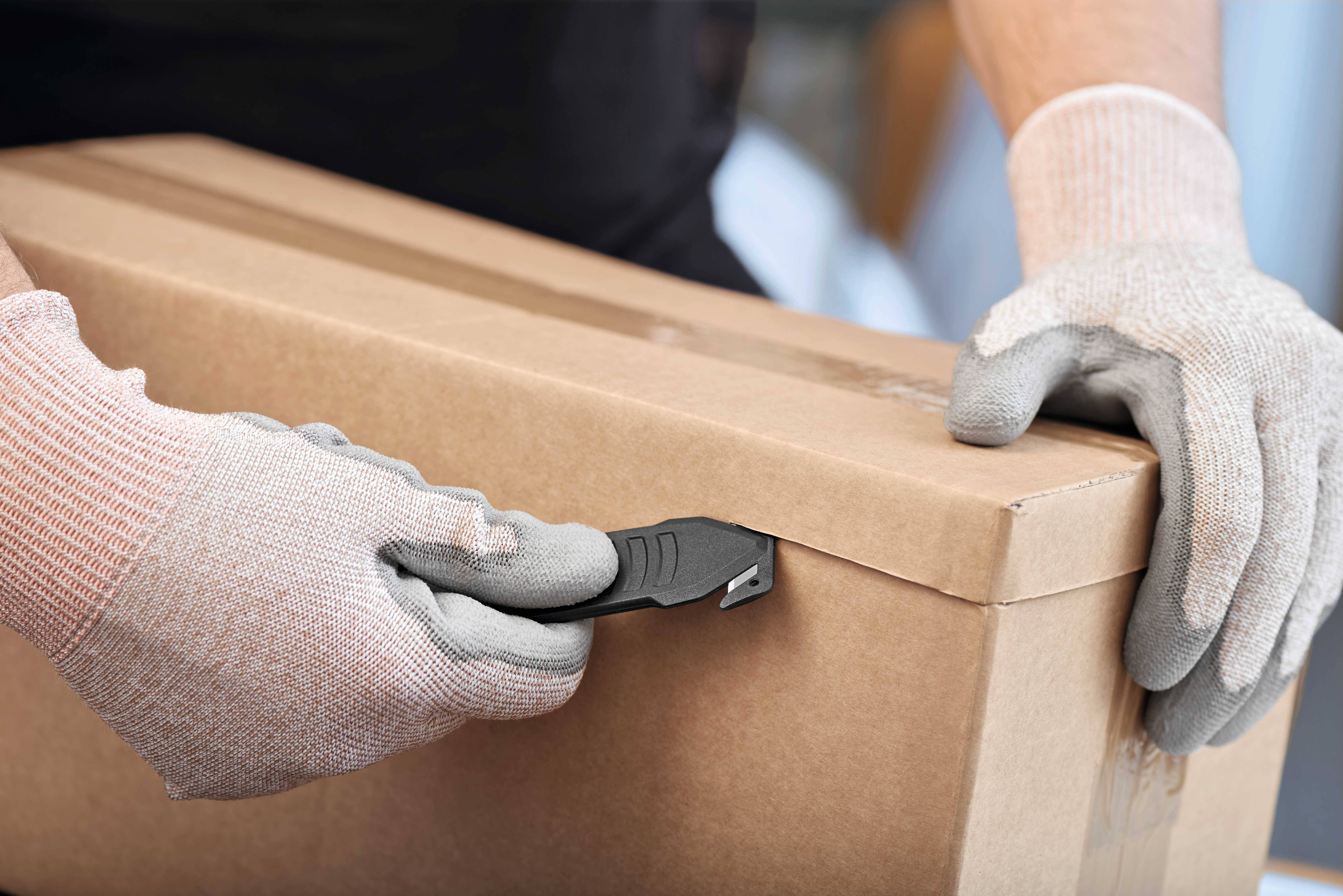 Eine Person öffnet vorsichtig einen Karton mit einem Cuttermesser. Sie trägt Handschuhe zum Schutz.