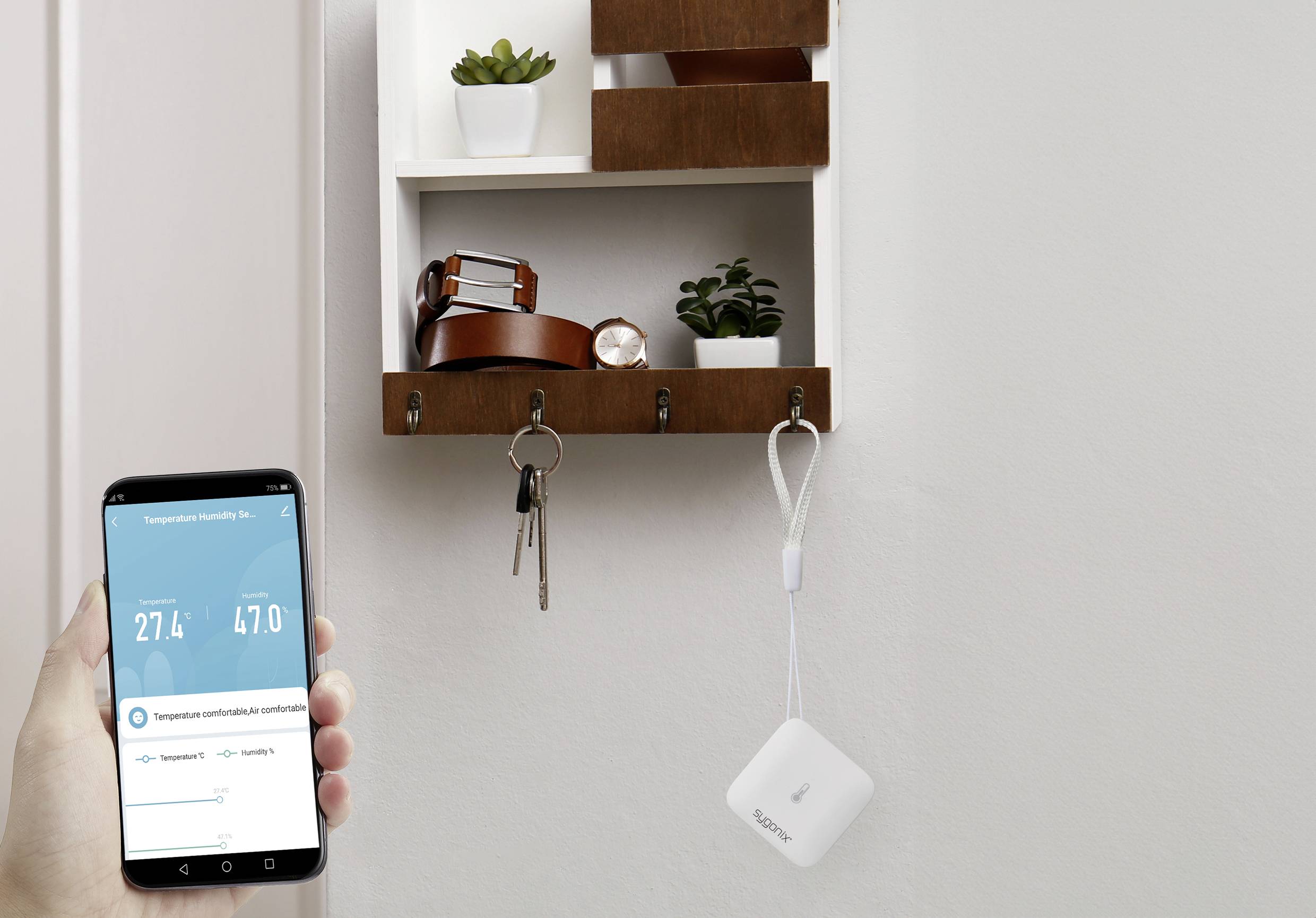 Person hält ein Smartphone mit einer App zur Temperatur- und Feuchtigkeitsüberwachung. Im Hintergrund Haken mit Schlüsseln und Regalfach.