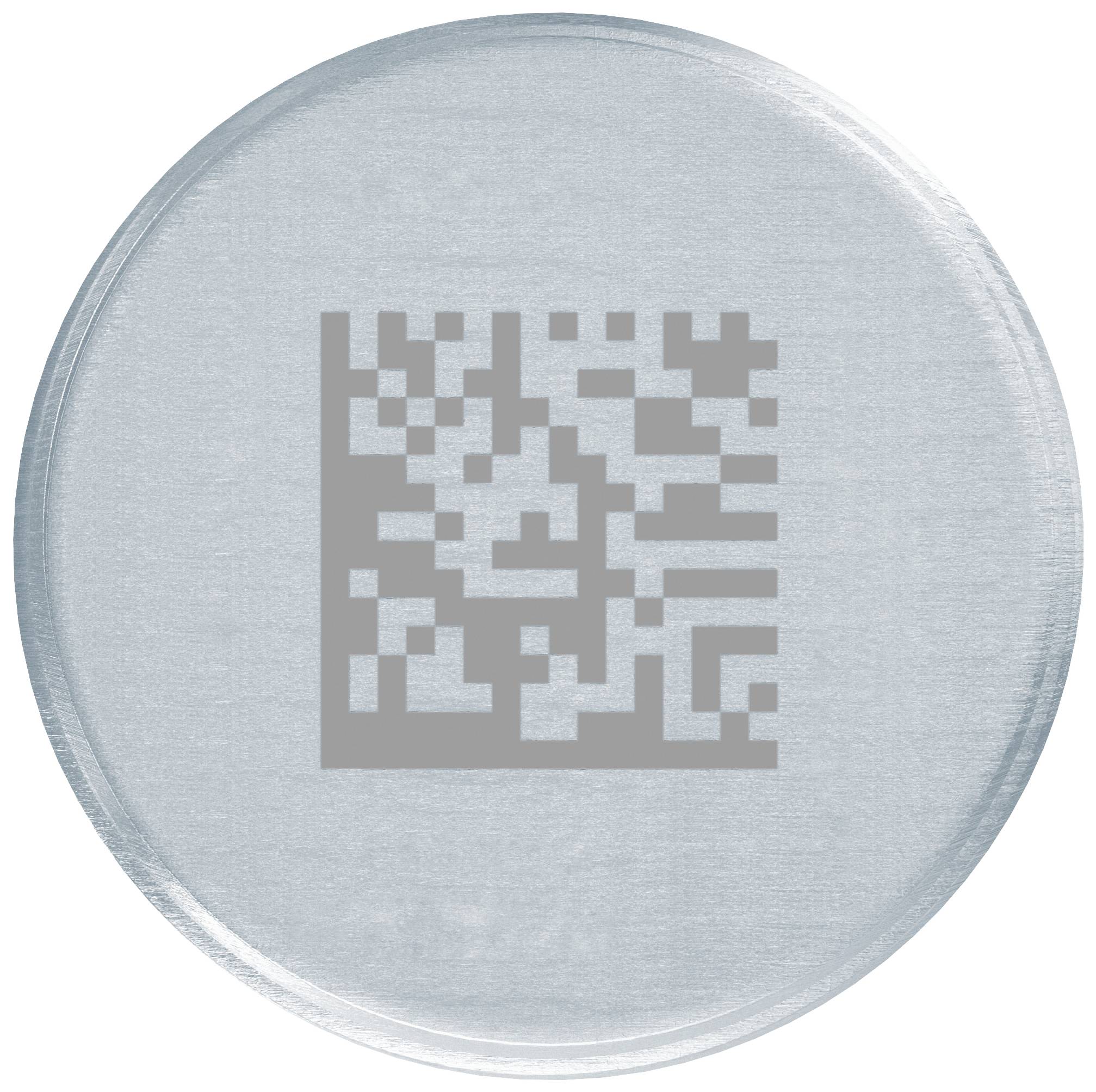 Ein silberner, runder Gegenstand mit quadratischem Muster in der Mitte, ähnlich einem QR-Code, auf einer weißen Fläche.