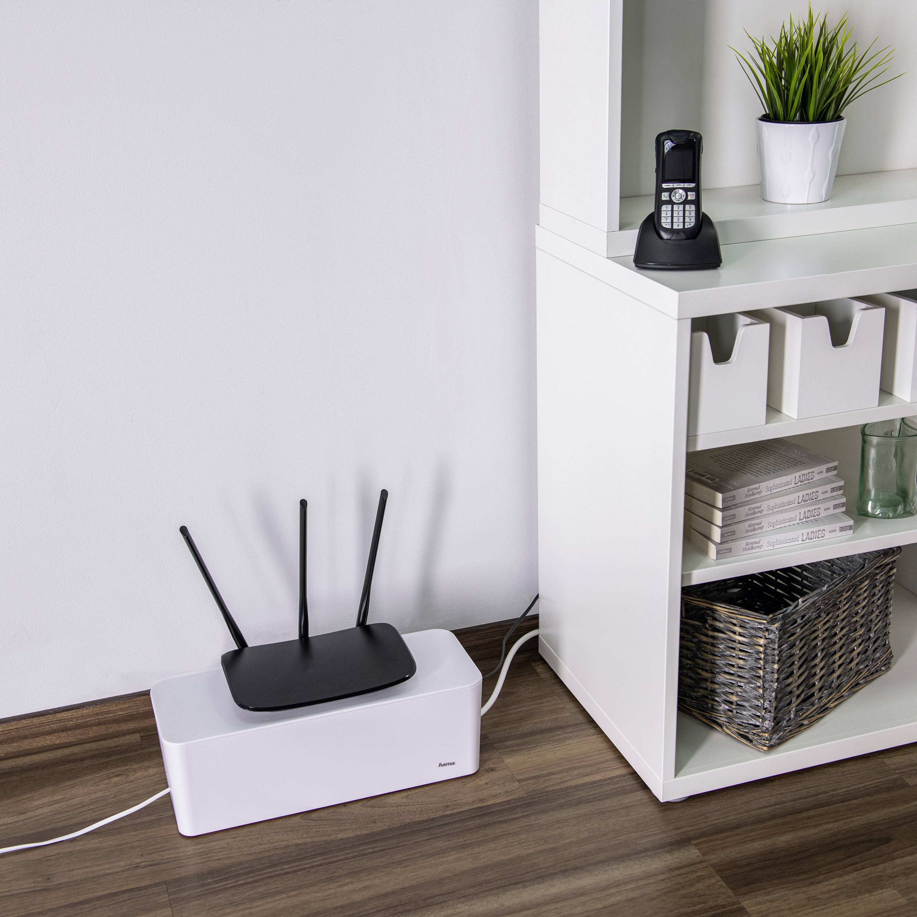 WLAN-Router steht auf einem Ablagefach neben einem Regal. Im Regal sind Bücher und Körbe ordentlich platziert.