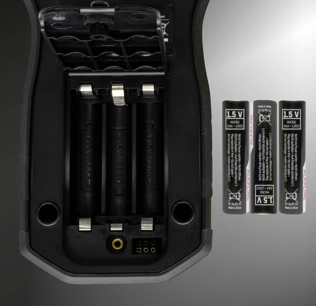 Offenes Batteriefach eines Geräts, das drei leere AA-Batteriefächer zeigt; daneben stehen drei AA-Batterien mit 1,5 V.