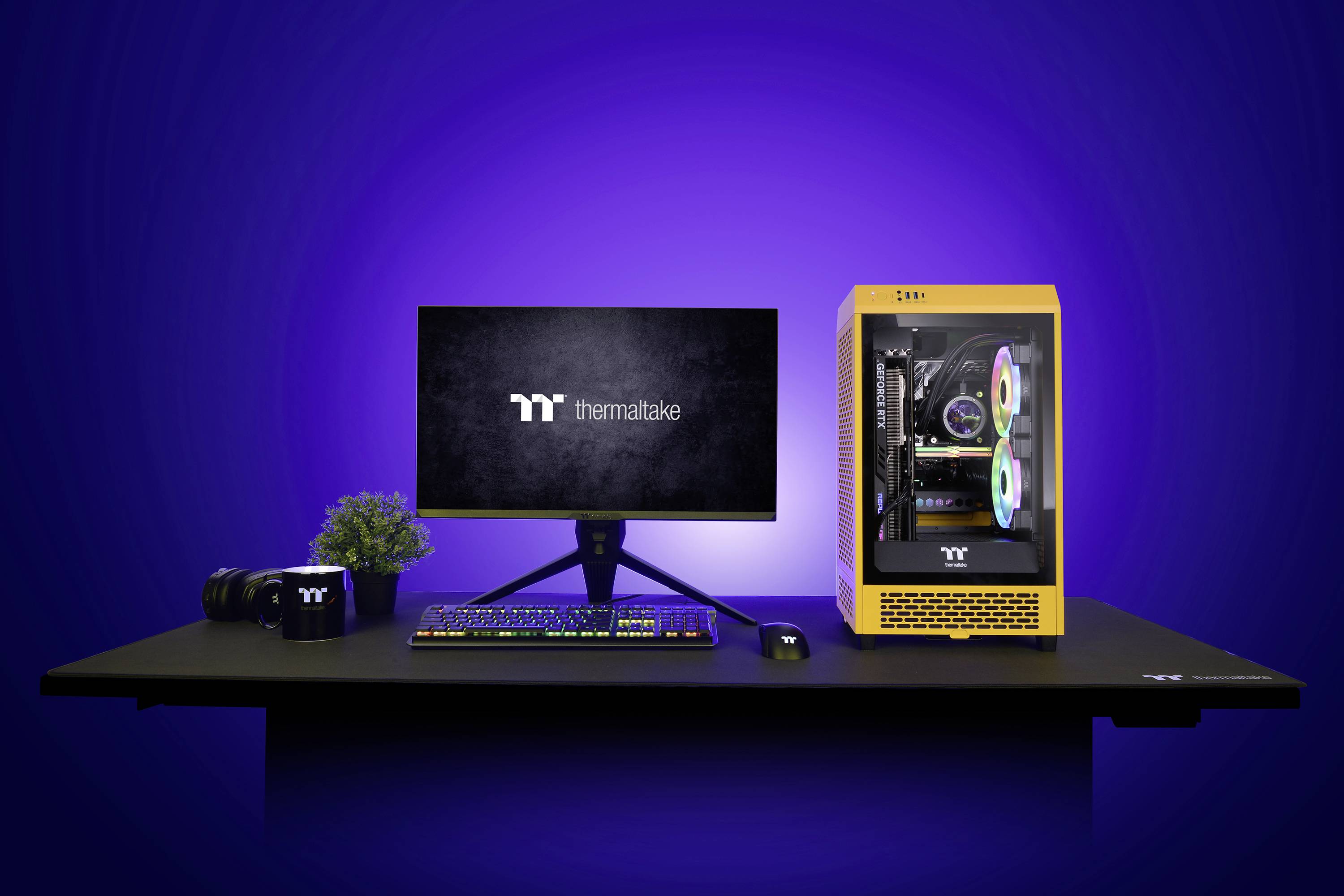 Ein gelber Computer mit beleuchtetem Inneren steht neben einem Monitor mit 'Thermaltake'-Logo, auf einem Computertisch mit Tastatur und Maus.